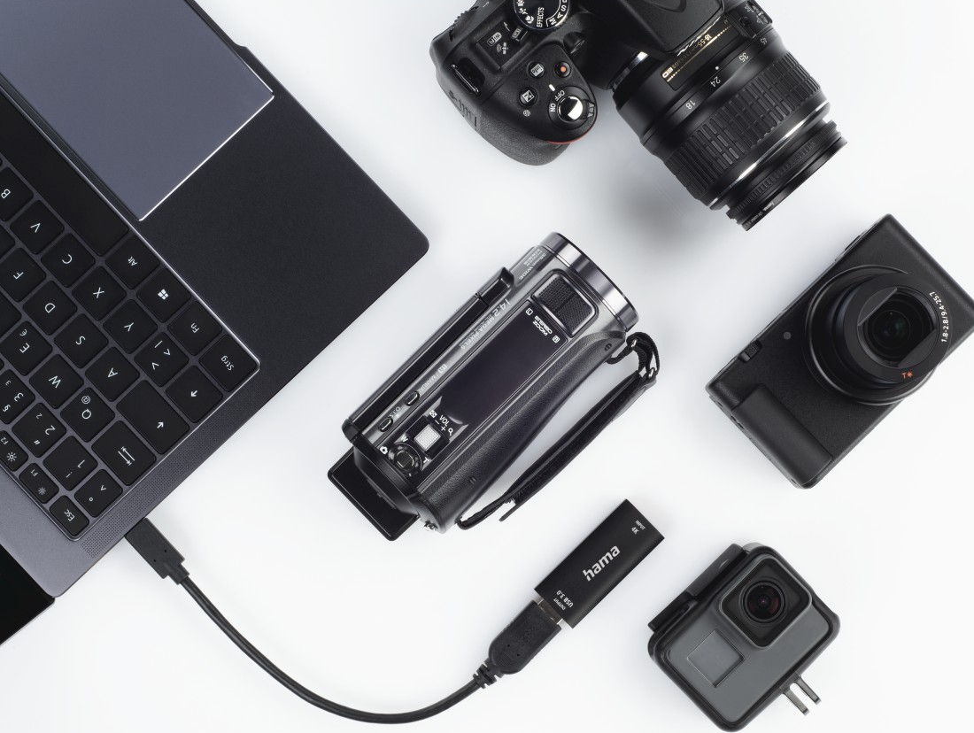 Laptop, fotocamera, videocamera e altri strumenti fotografici su una superficie bianca.