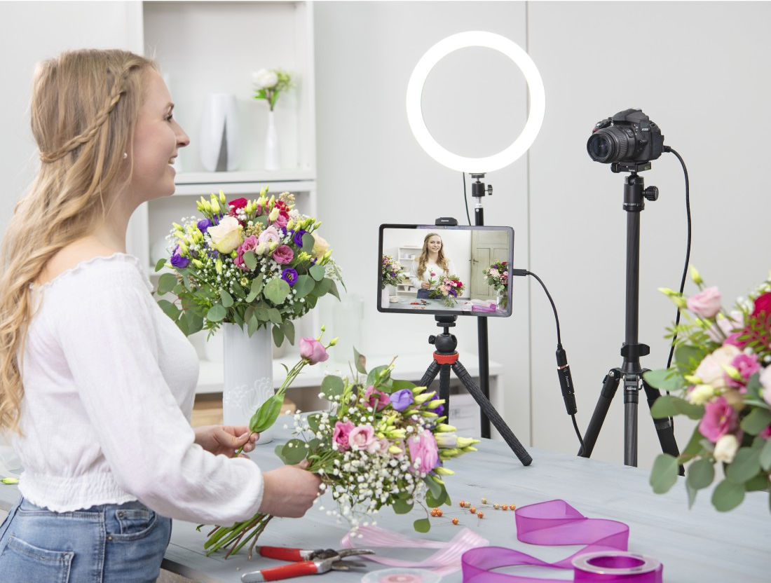 Una donna sta filmando un tutorial di composizione floreale con una luce ad anello e una fotocamera.
