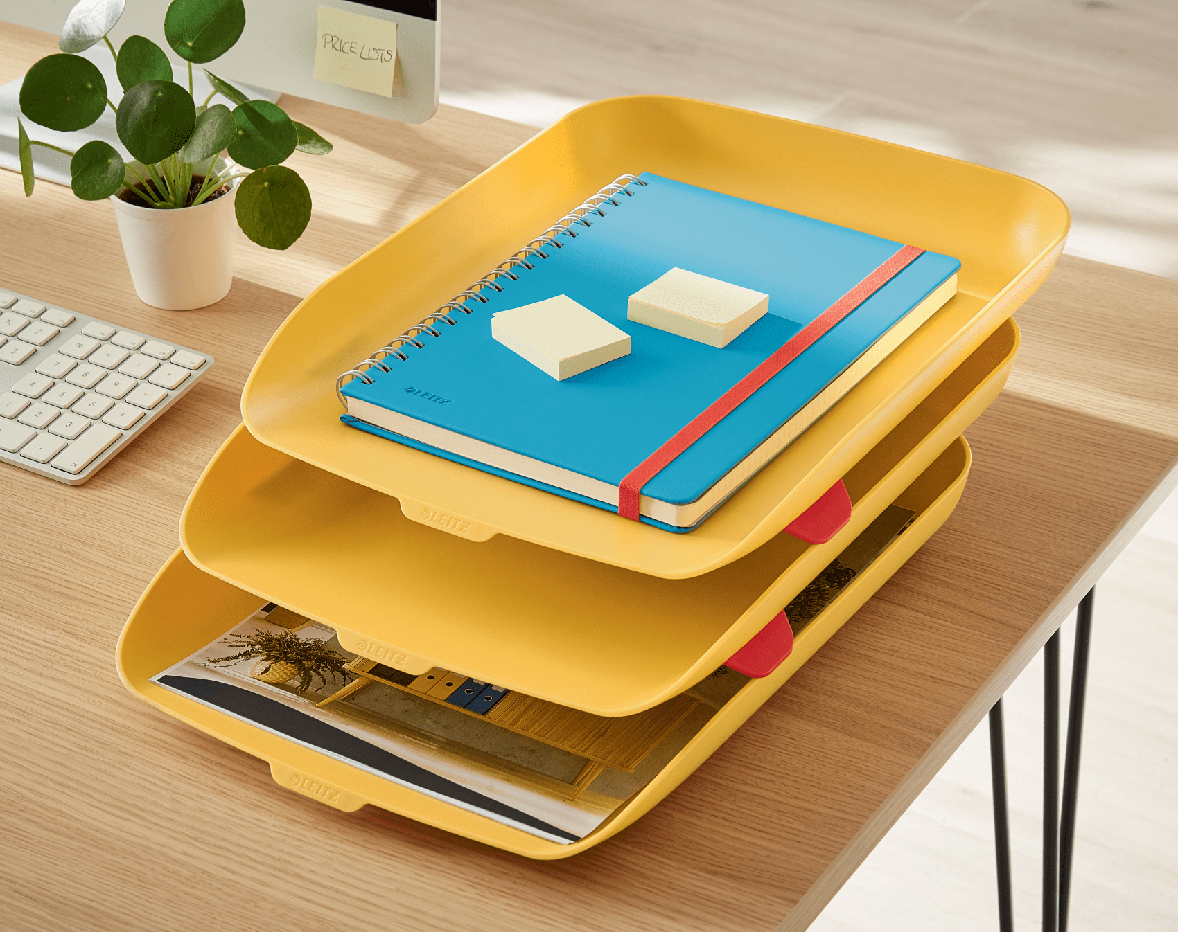 Sárga tálcák kék jegyzetfüzettel, post-it-ekkel és dokumentumokkal egy fa íróasztalon.