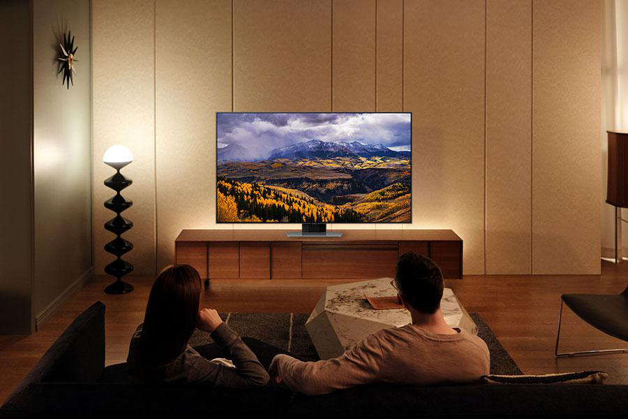 Paar auf Couch, schaut Fernseher mit Landschaftsbild.