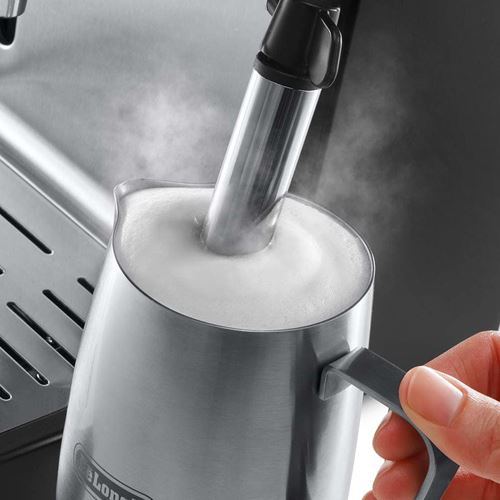 Una jarra espumadora de leche de acero inoxidable con vapor saliendo. Una mano sostiene el mango.
