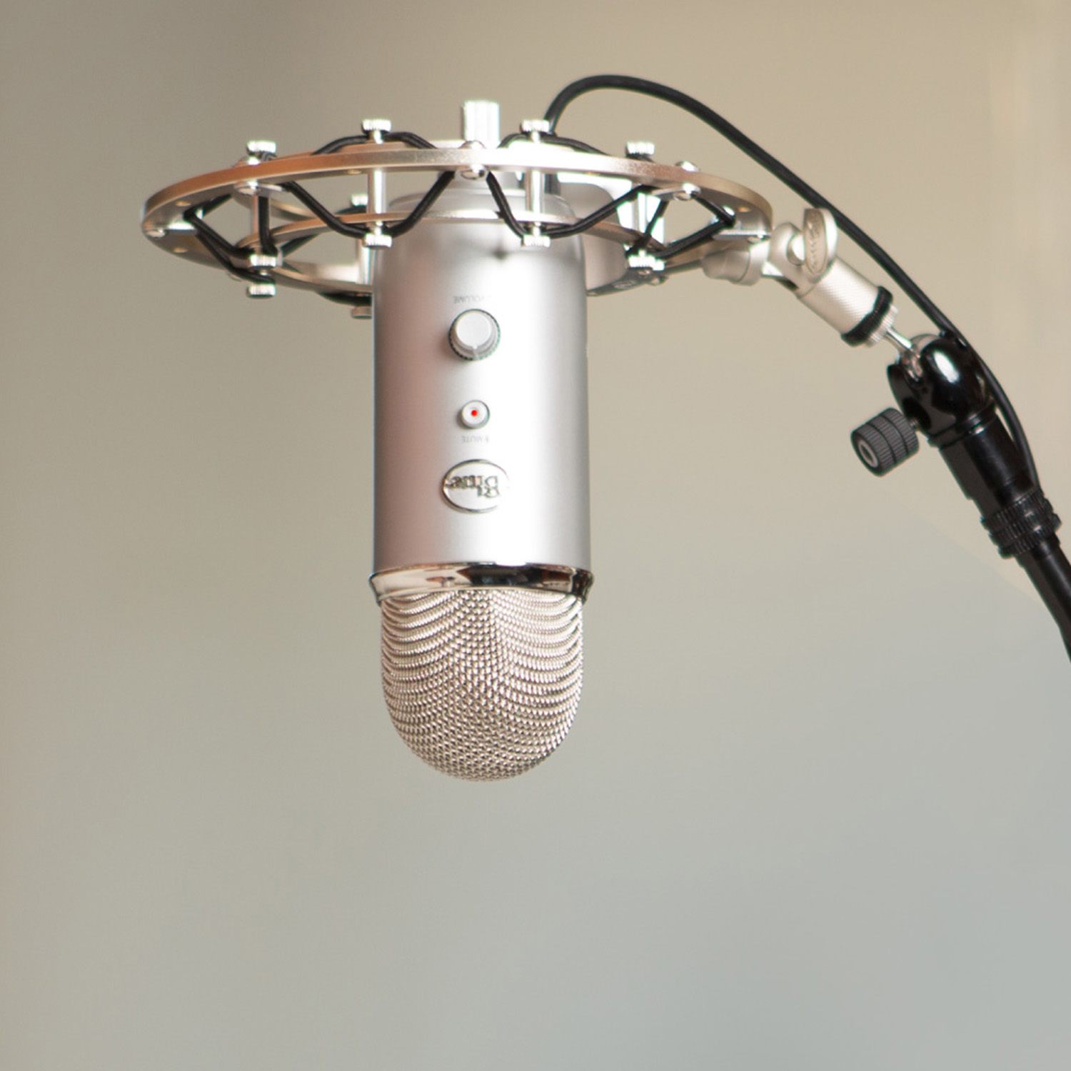 Ein silbernes Blue Yeti Mikrofon ist aufgehängt. Es hängt an einem runden silbernen Rahmen, der von einem schwarzen Ständer getragen wird. Der Hintergrund ist neutral.