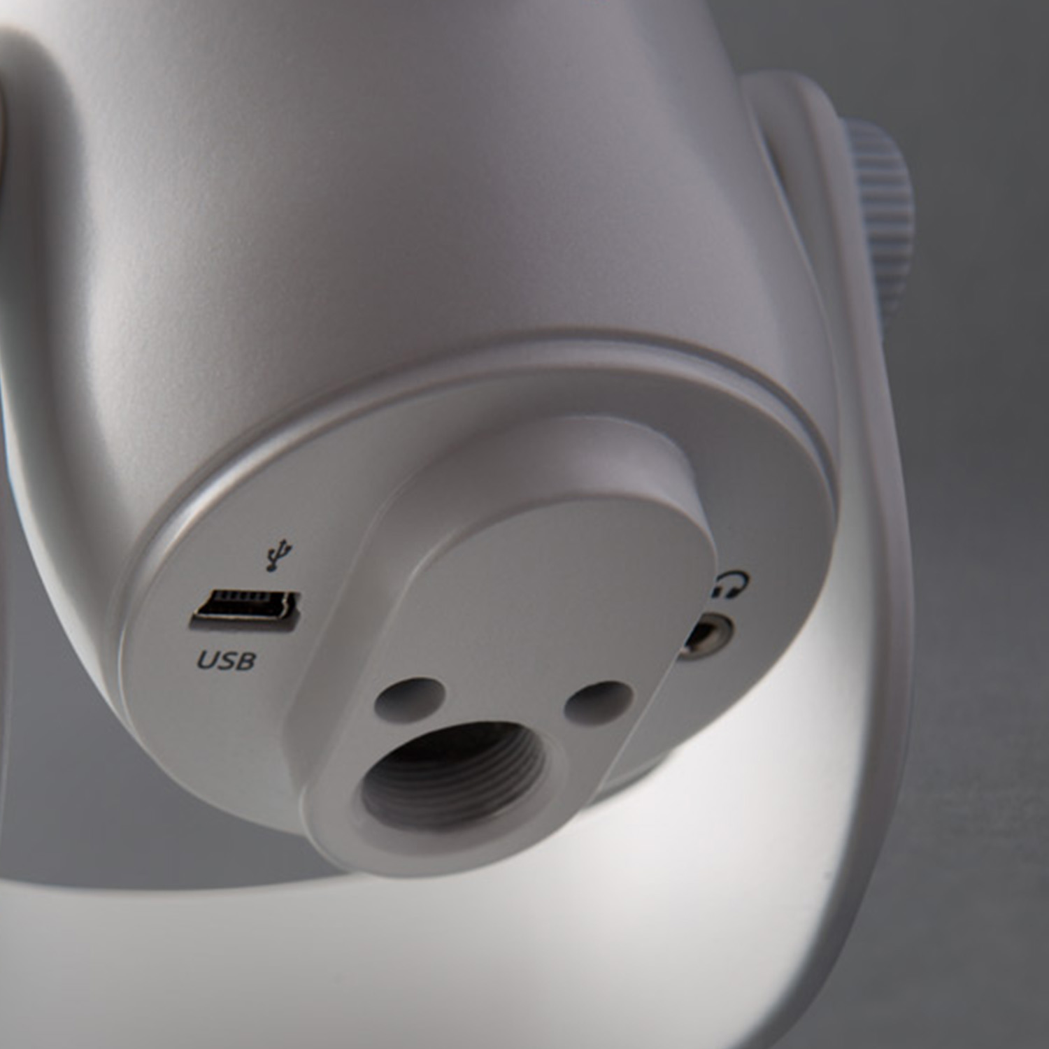 Nahaufnahme eines weißen Mikrofonfußes mit USB-Anschluss und Kopfhöreranschluss. Der Sockel hat ein Schraubgewinde und einen Ein-/Ausschalter.