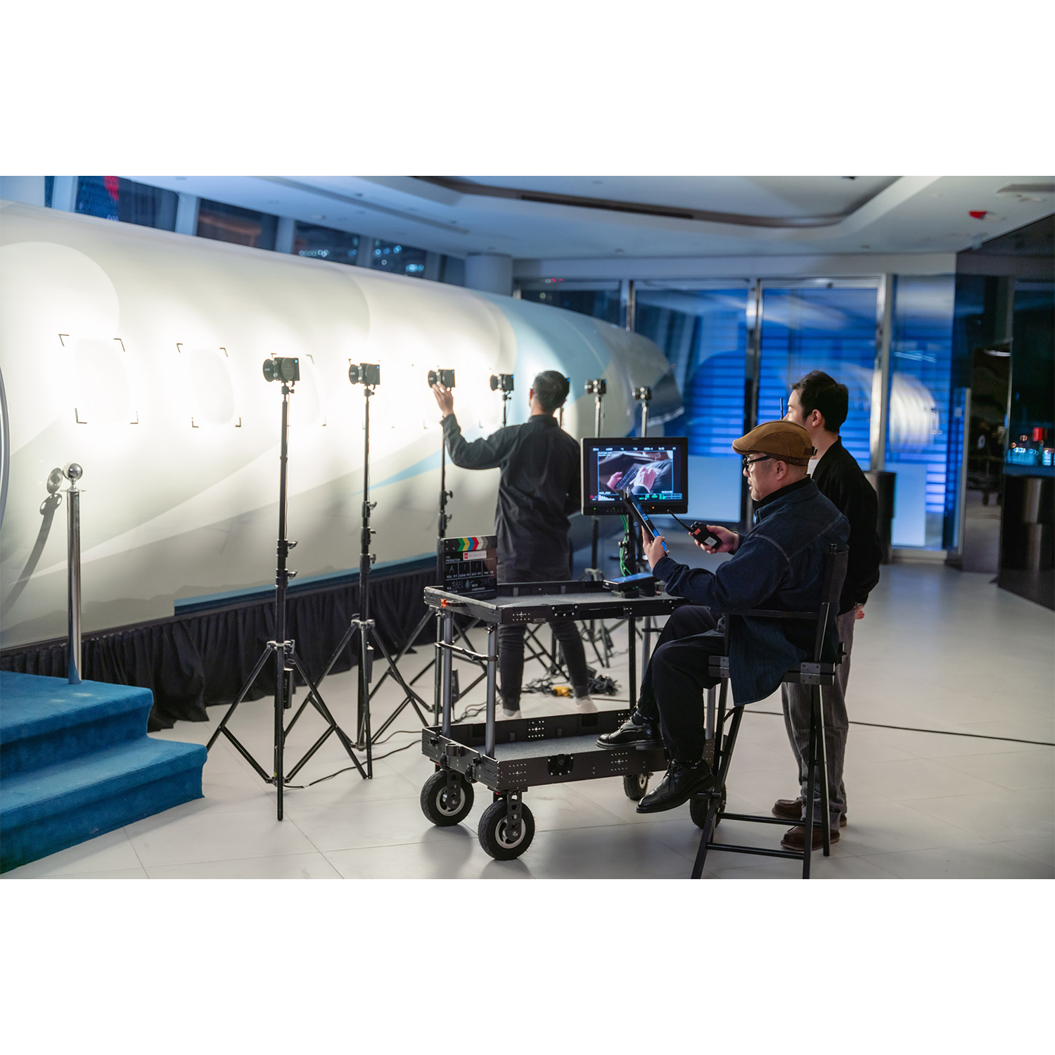 Troupe cinematografica che configura telecamere e monitora le attrezzature in uno studio con un grande oggetto bianco.