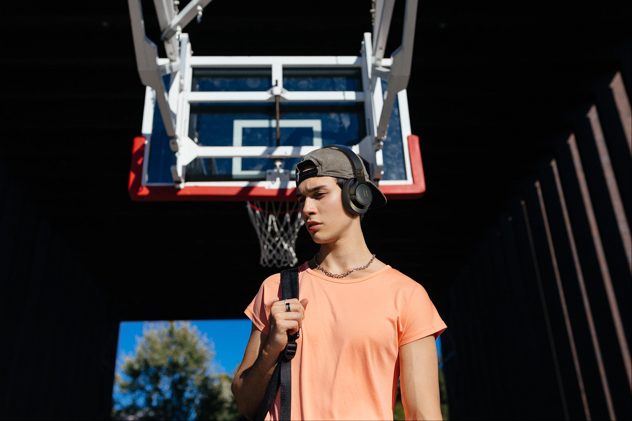 Ein junger Mann in einem orangefarbenen Hemd und einer Kappe steht vor einem Basketballkorb.