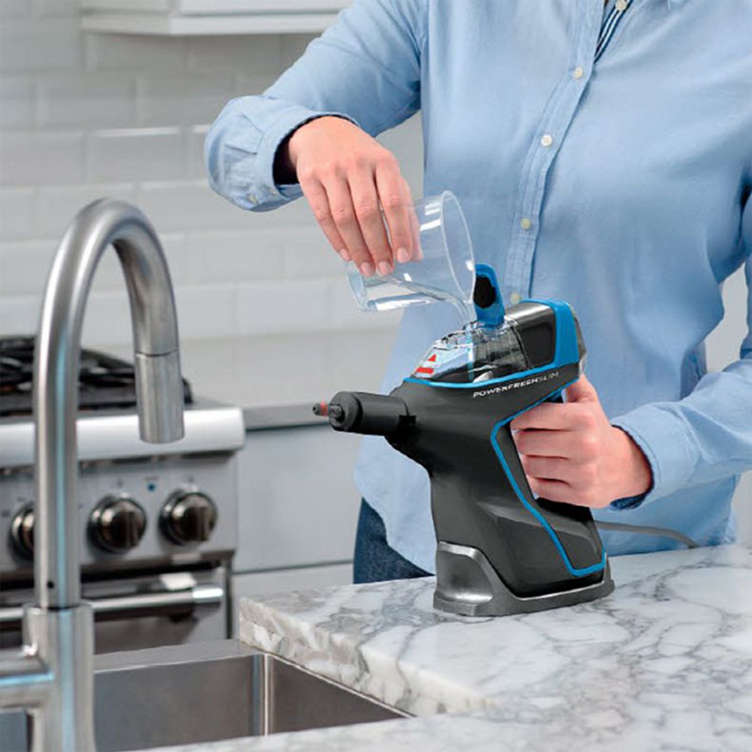 Una persona versa acqua in un pulitore a vapore nero e blu tenuto su un piano di lavoro bianco. Un lavandino è visibile.