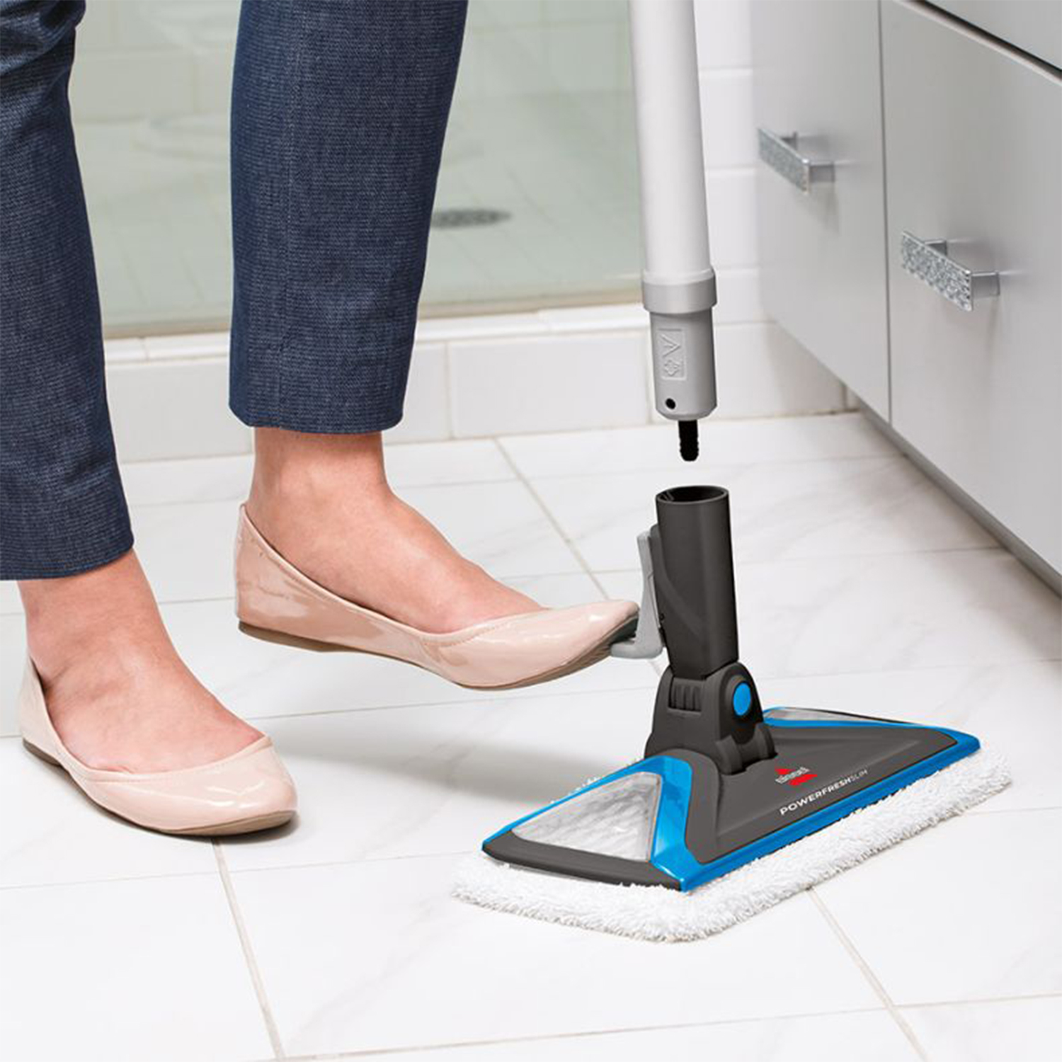 Piedi di donna e una scopa Bissell Powerfresh. Il mocio viene assemblato su un pavimento di piastrelle bianche.
