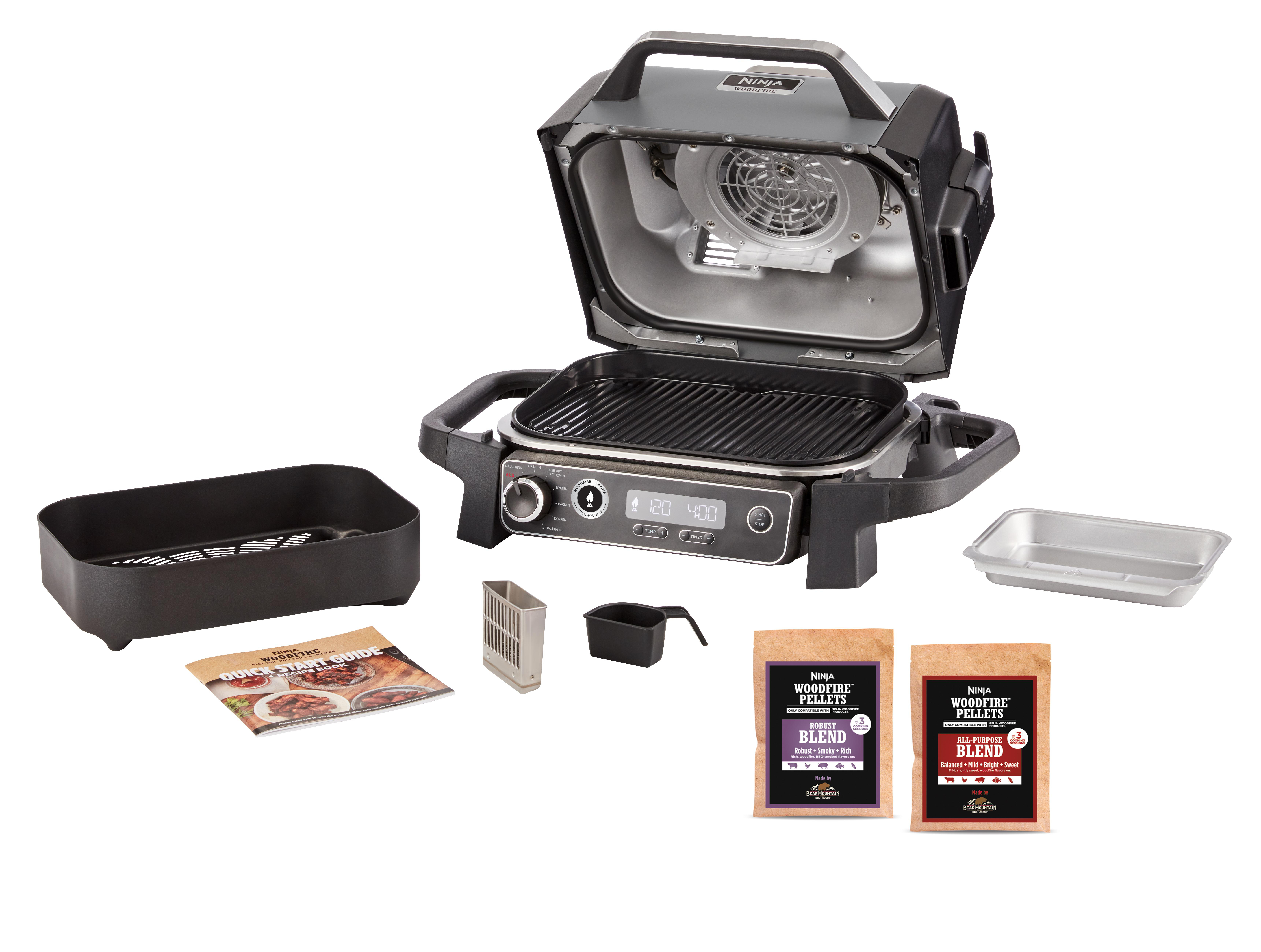 Ein Ninja Woodfire Grill, geöffnet, mit Zubehör und Woodfire Pellets auf weißer Oberfläche.