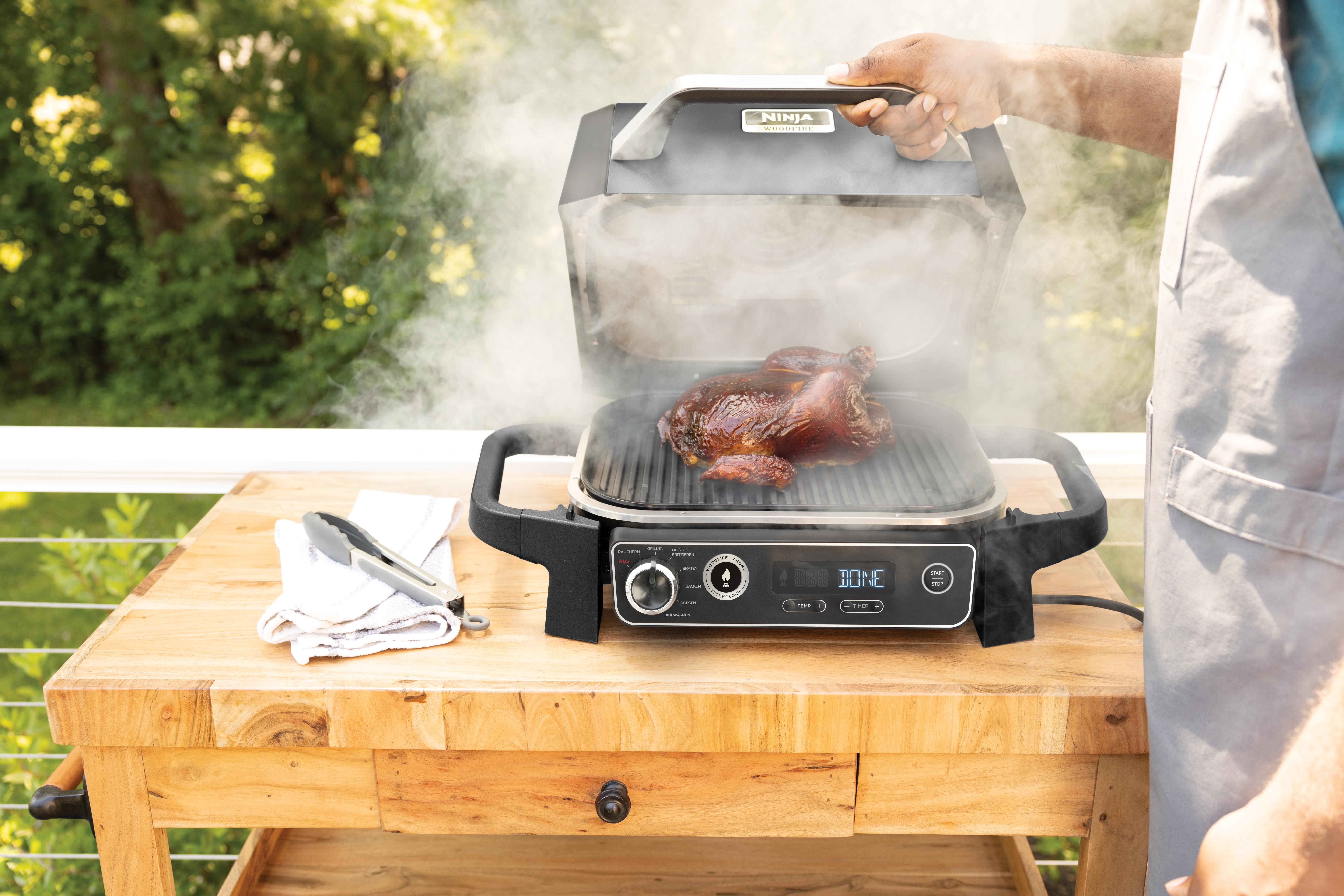Ein Grill mit Rippchen und gegrillten Rippchen auf einem Holztisch mit Gewürzen und Paprika.