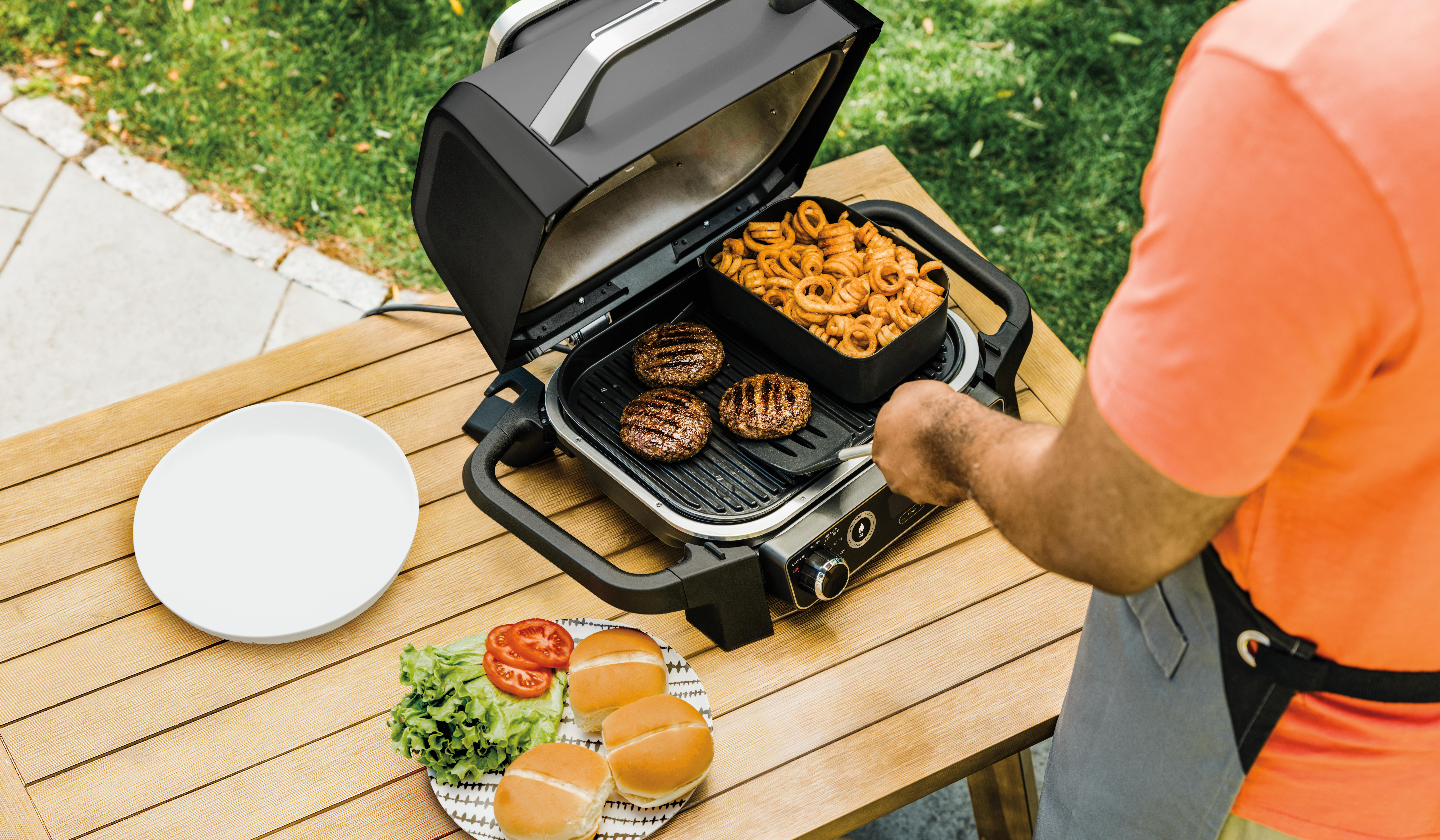 Eine Person grillt Burger und Beilagen im Freien.