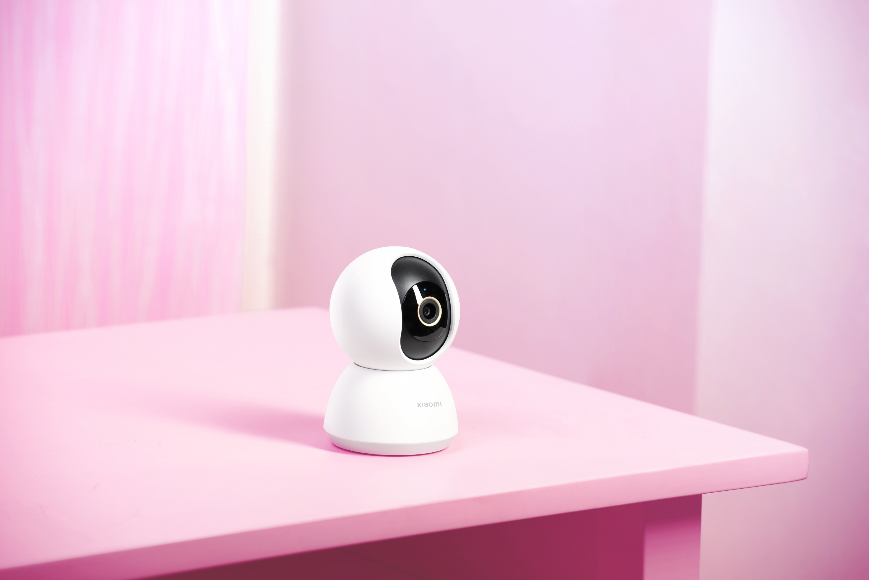 Telecamera di sicurezza bianca su un tavolo rosa, davanti a un muro rosa.
