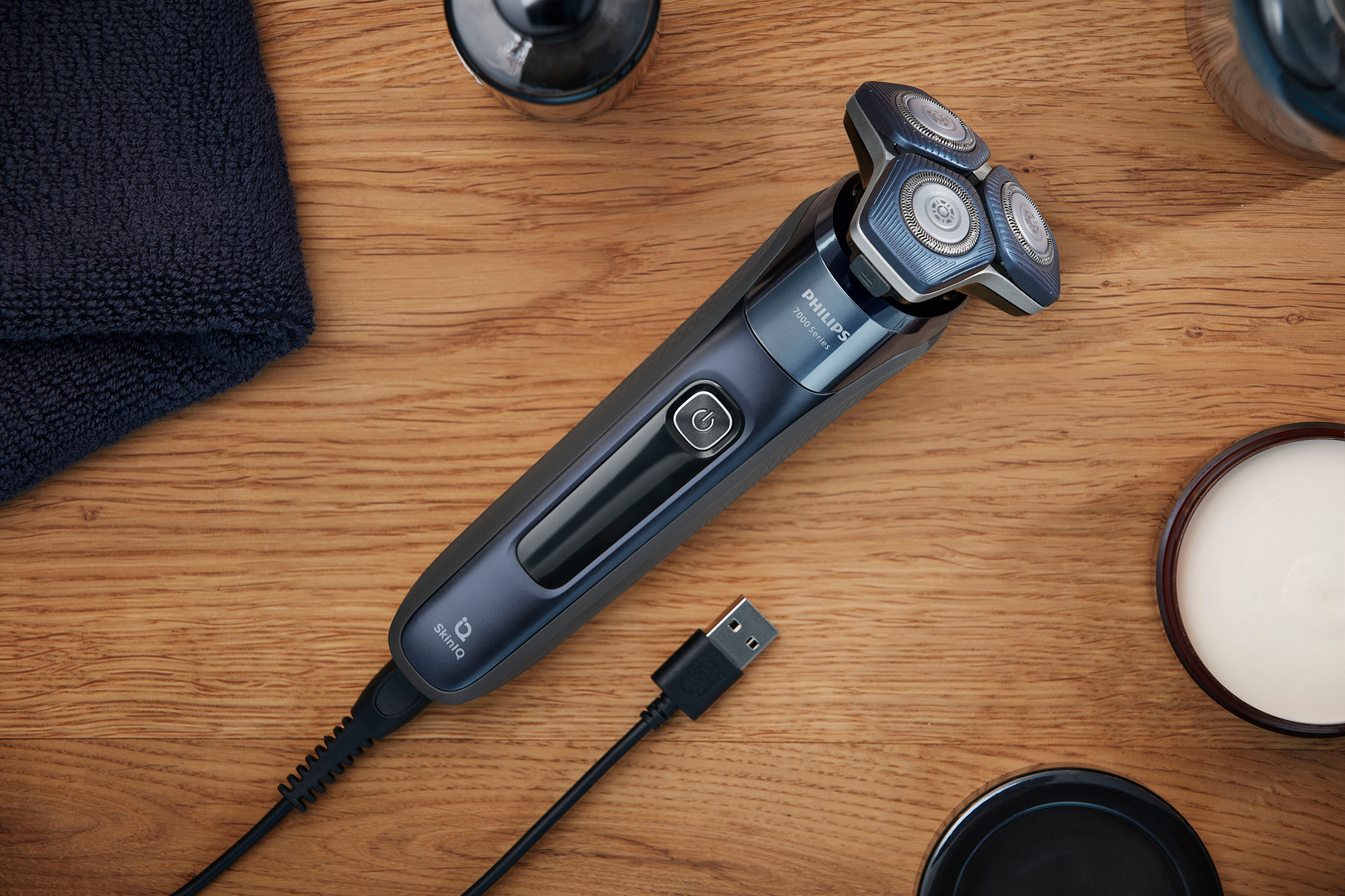 An electric shaver with a dark blue handle and three rotating heads on a wooden table.