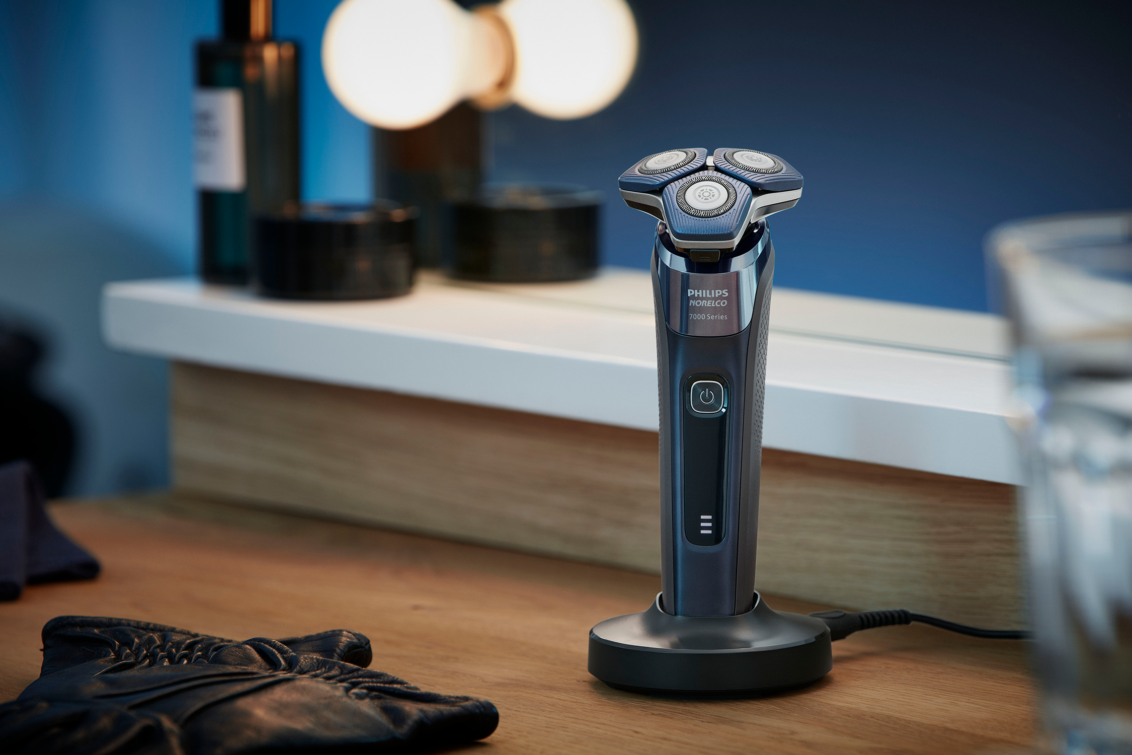 Electric shaver with charging stand and a black leather glove on a wooden surface.