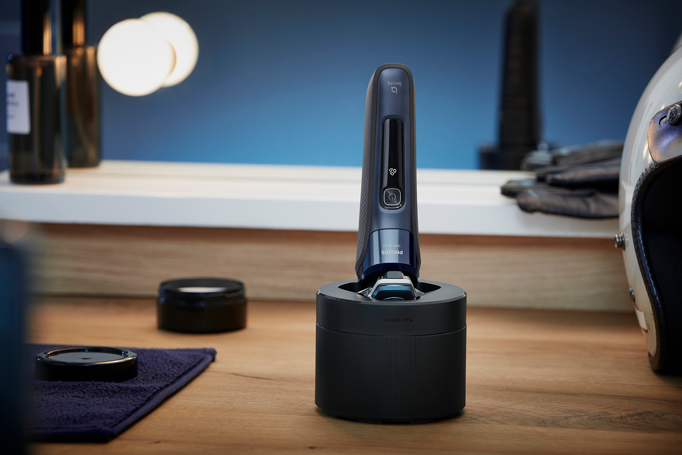 A black Philips shaver in a charging station. The background shows bathroom items and a mirror.