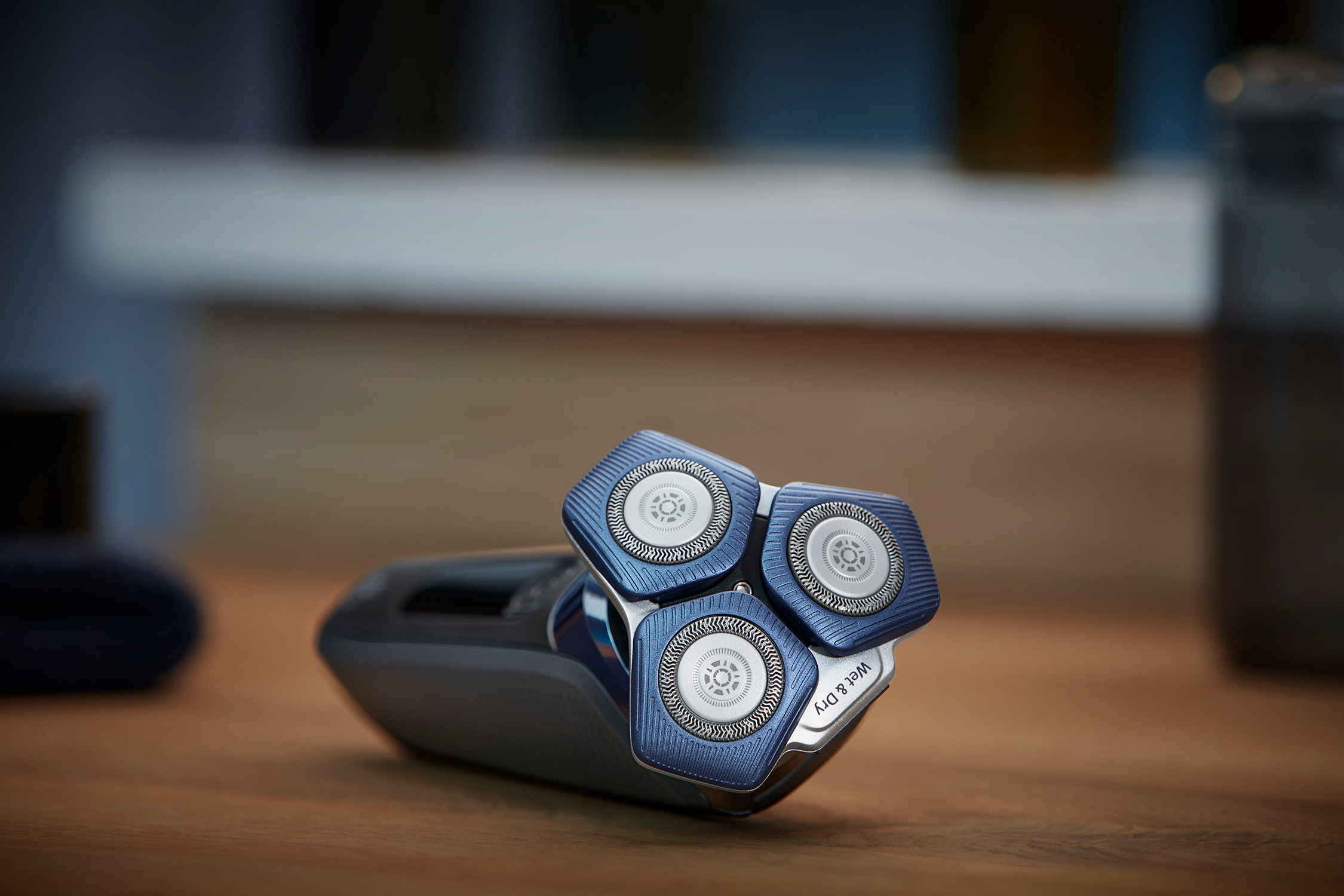 A close-up of a blue and silver electric shaver with three rotating heads, on a wooden surface.