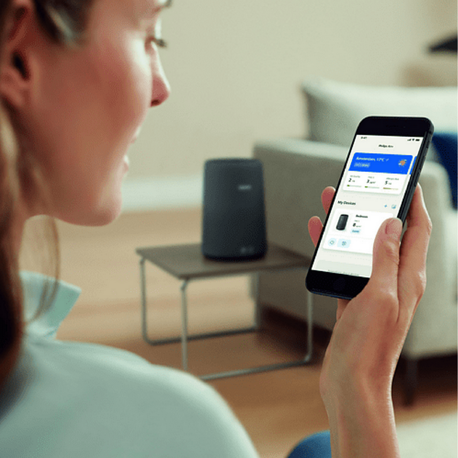 Femme tenant un smartphone, regardant un haut-parleur intelligent sur une table d'appoint.