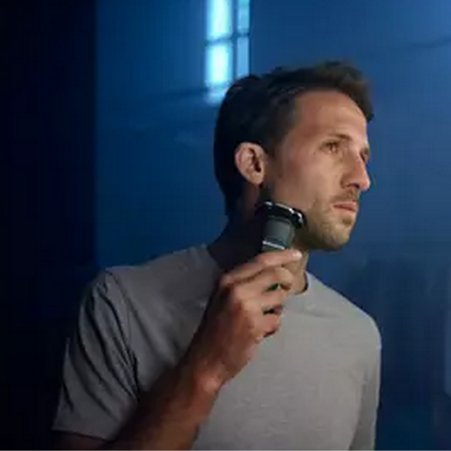 A man shaves his face with a Philips electric shaver. Dark blue background.