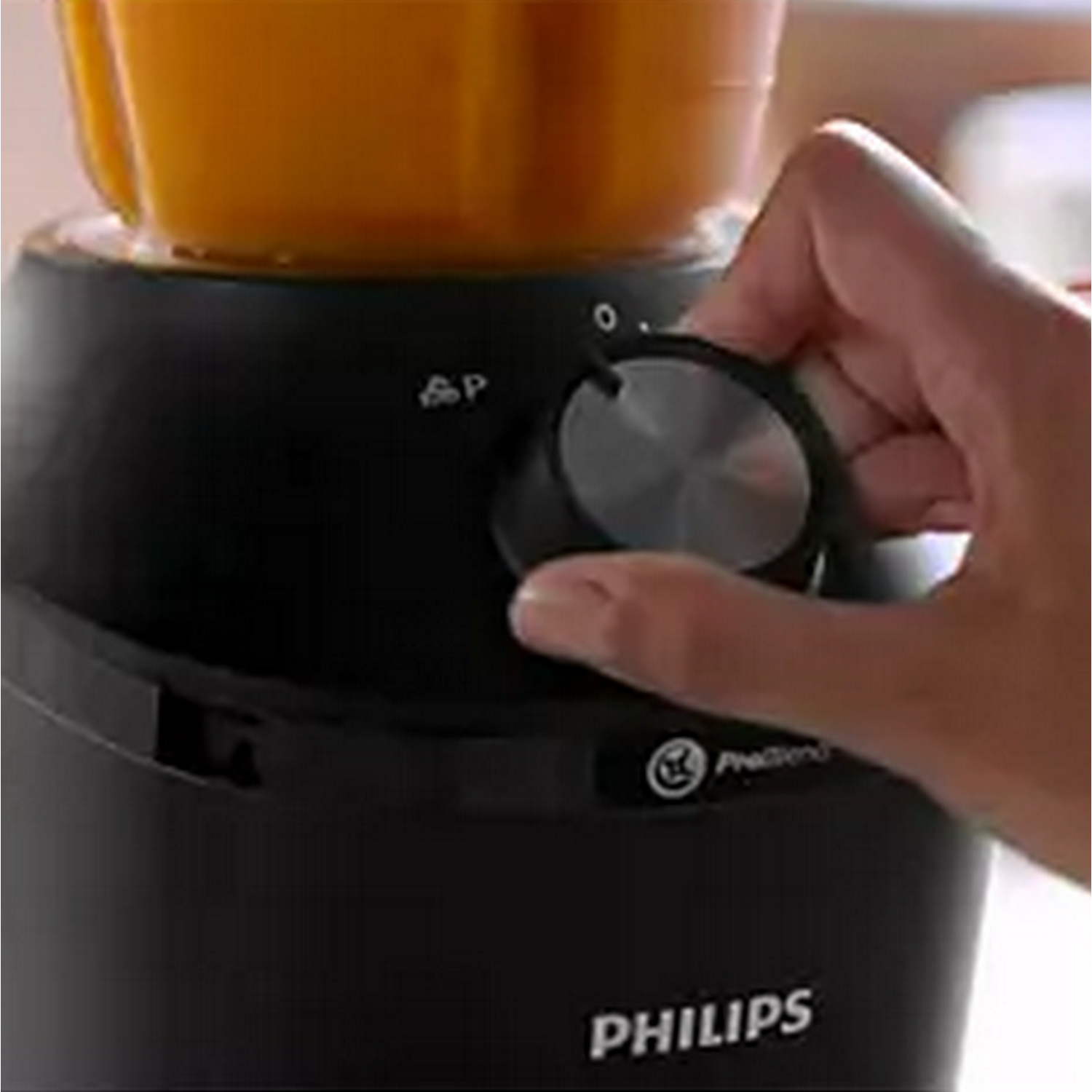 Hand turning the dial on a black blender, with an orange liquid inside.
