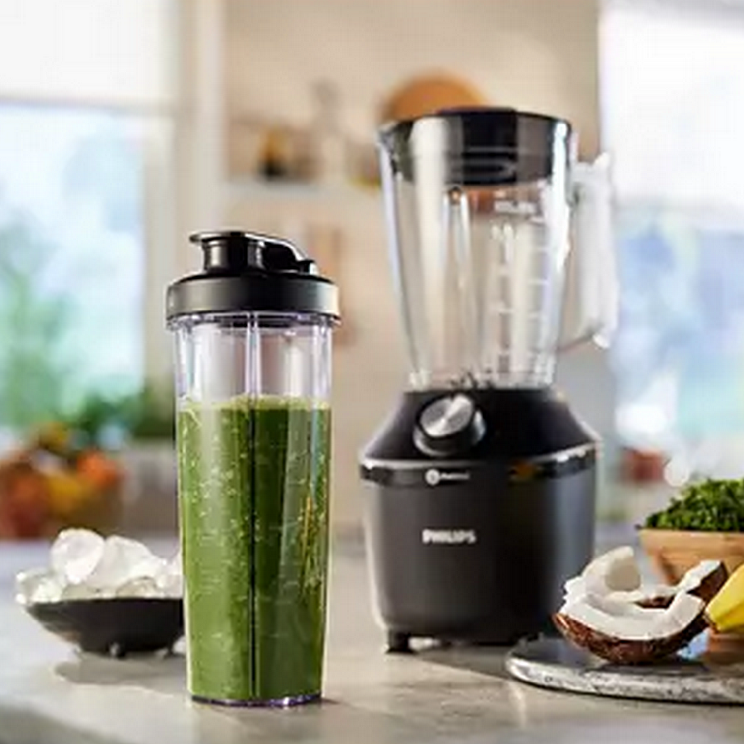 Blender and a green smoothie in a cup with ice and coconut on the counter.