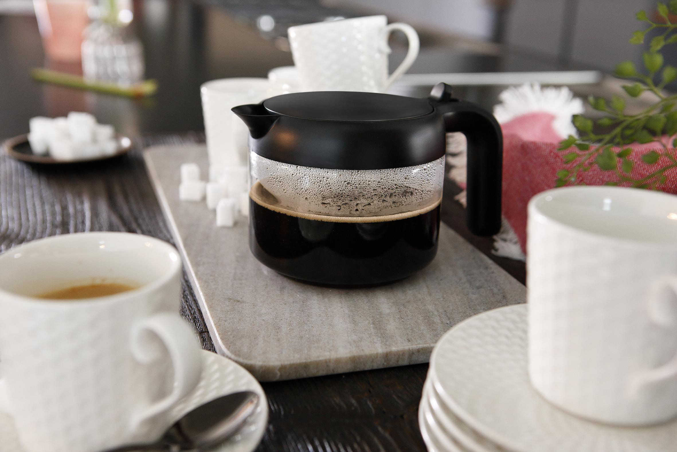 Kaffeemaschine mit Kaffee, Zuckerwürfeln und weißen Tassen auf einem Holztisch.