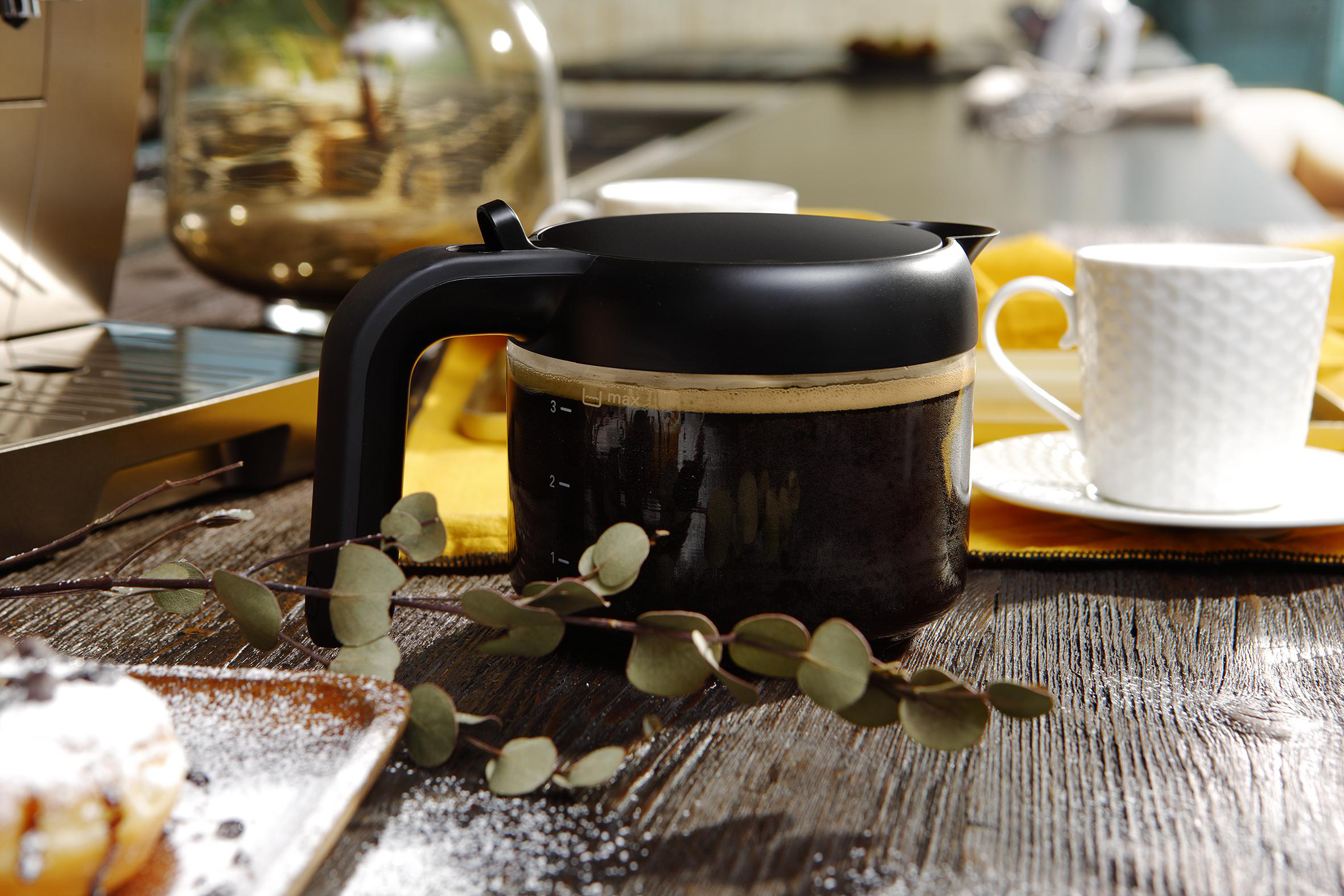 Eine schwarze Kaffeekanne mit Kaffee, eine weiße Tasse und ein Holztisch mit einigen Pflanzen.