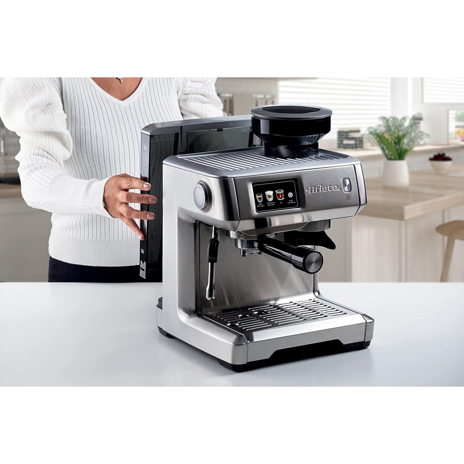 Macchina per caffè espresso in acciaio inossidabile con una donna che la aziona sullo sfondo.