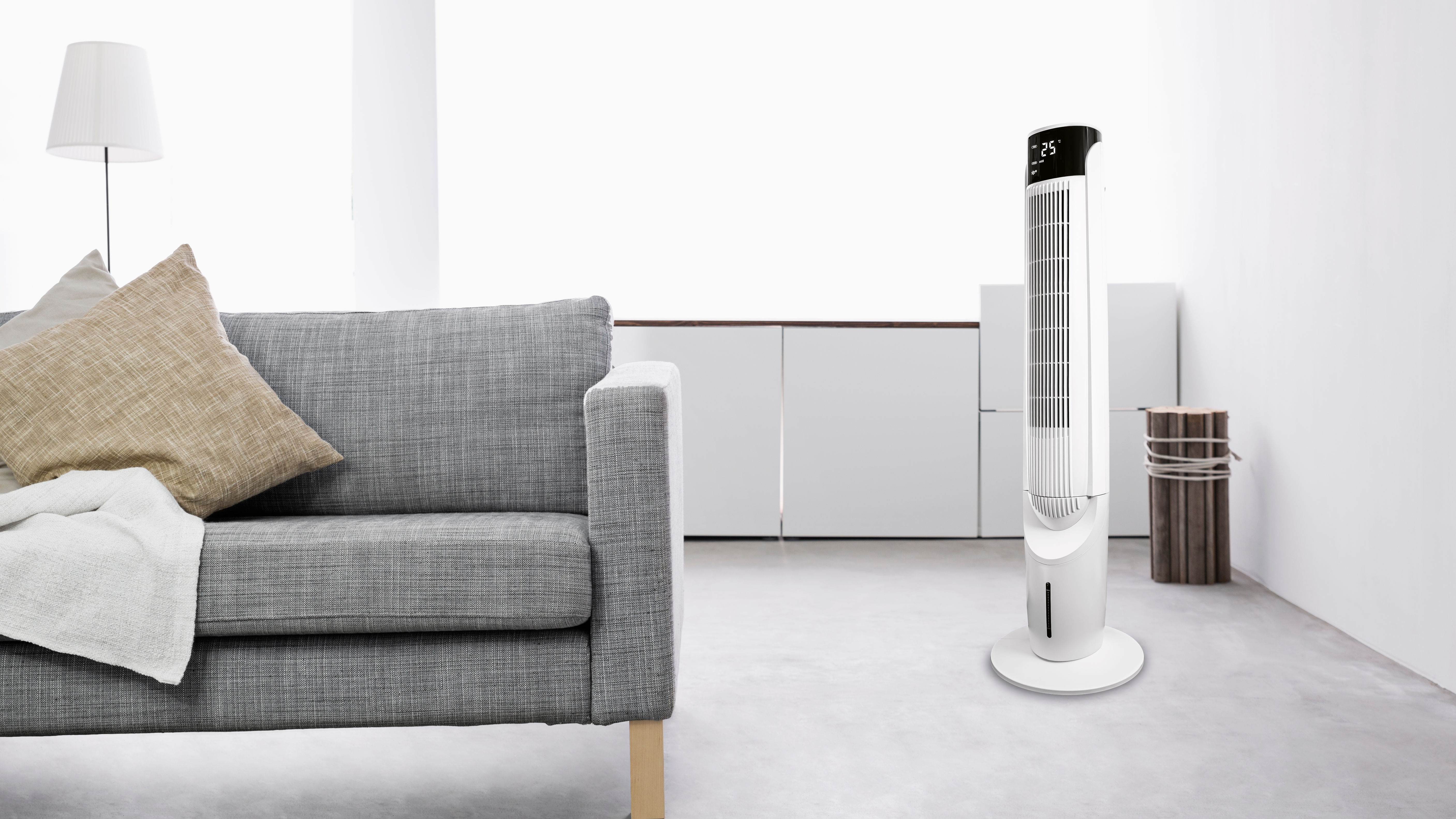 Weißer und schwarzer Luftkühler mit weißem Sockel, neben einem grauen Sofa und einer Lampe.