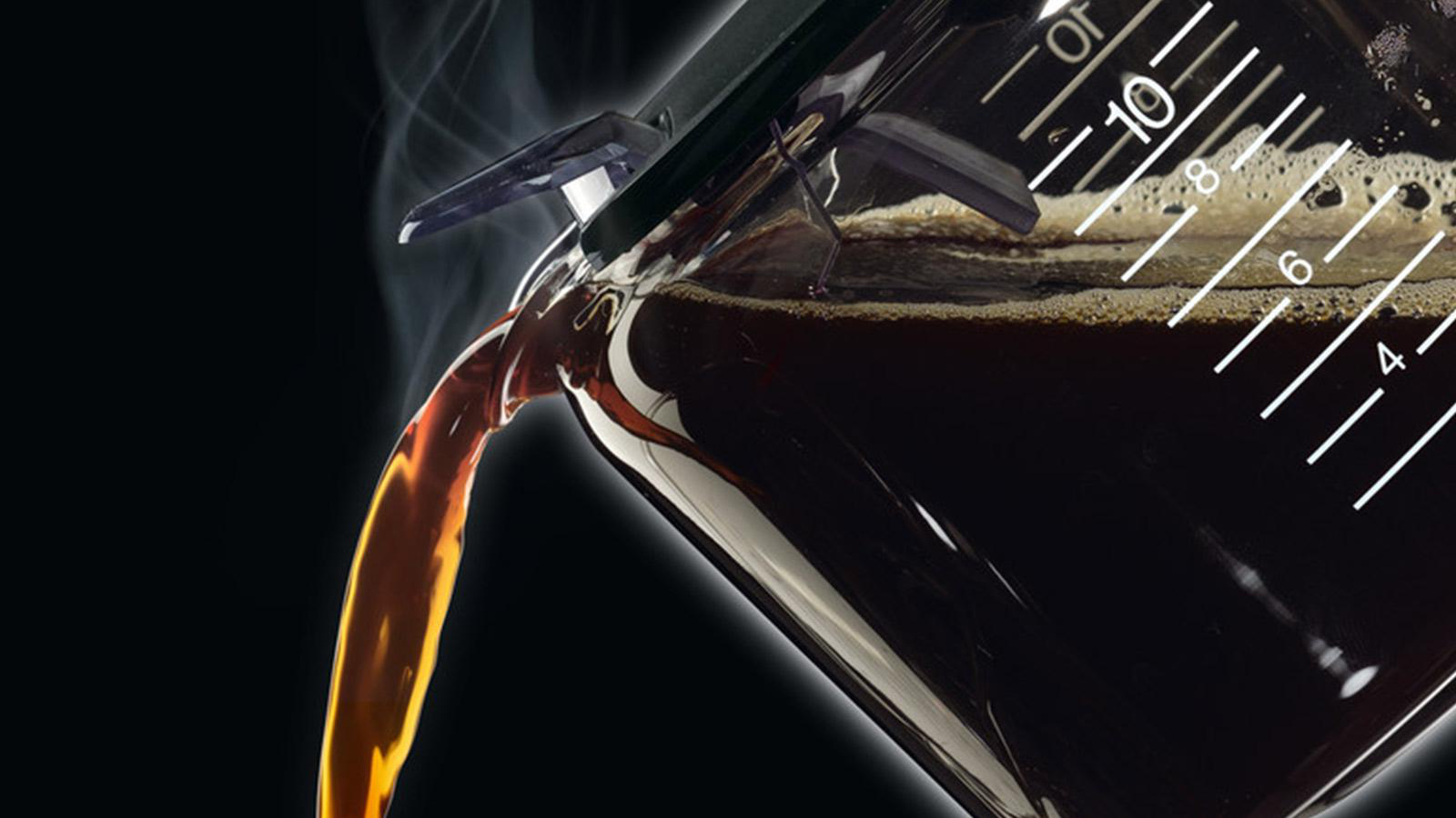 Nahaufnahme von Kaffee, der aus einer Glaskaraffe gegossen wird. Dampf steigt auf, die Flüssigkeit ist dunkelbraun.