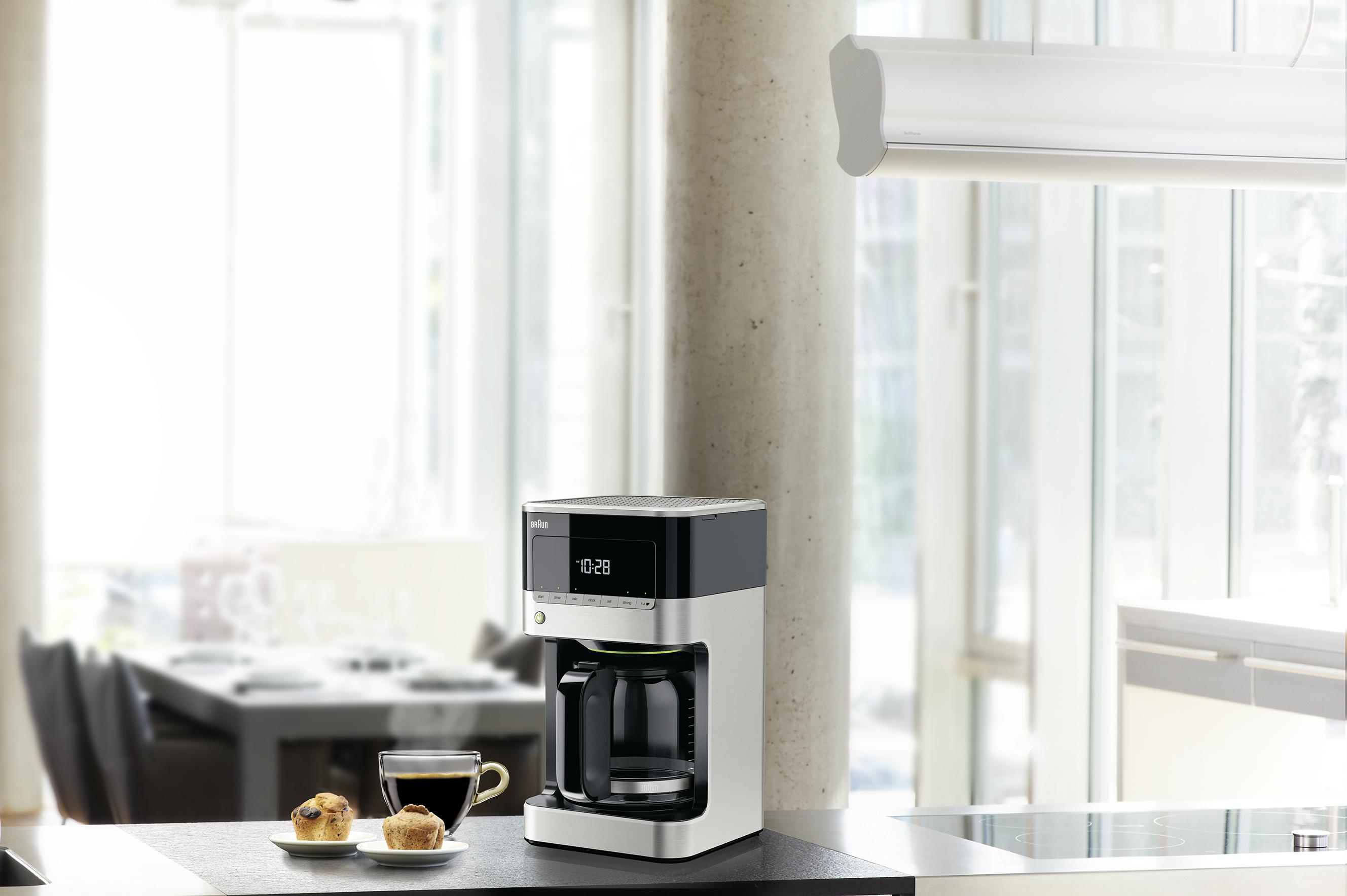 Küchenszene: Kaffeemaschine, Tasse, Muffins auf einer Theke und verschwommener Hintergrund eines Fensters.