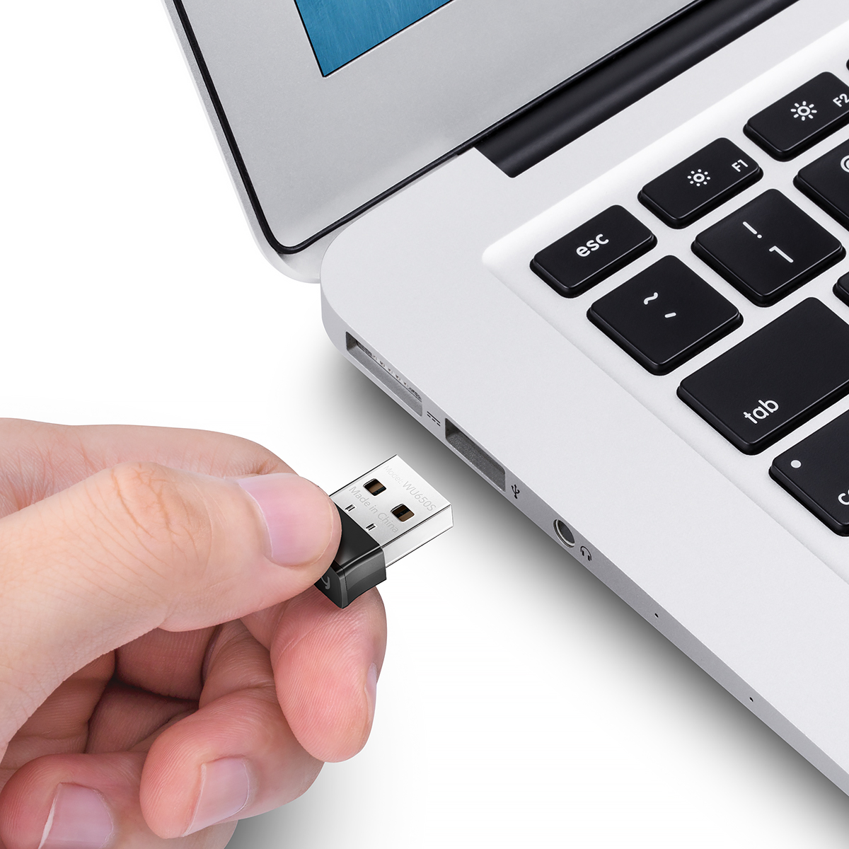 Kézben egy fekete-ezüst USB-meghajtó, egy ezüst laptop mellett, a billentyűzet közelében. A meghajtó behelyezés előtt áll.