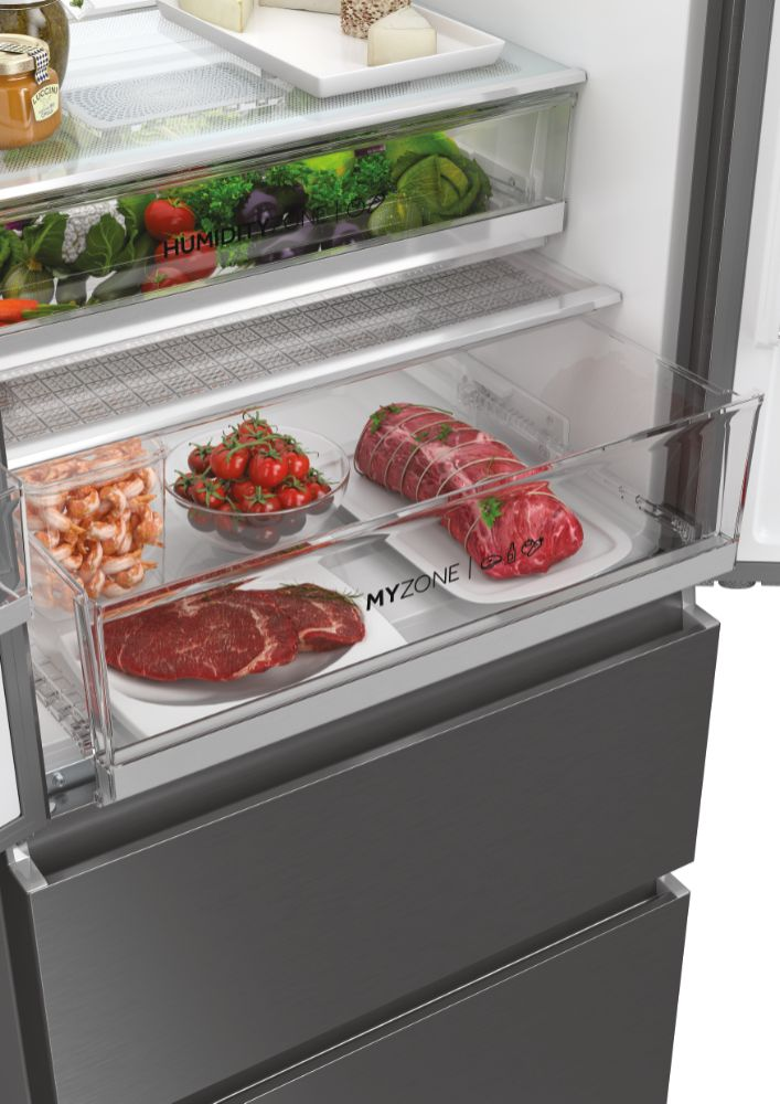 Primo piano dell'interno di un frigorifero con cassetti pieni di alimenti come pomodori, carne e gamberi.