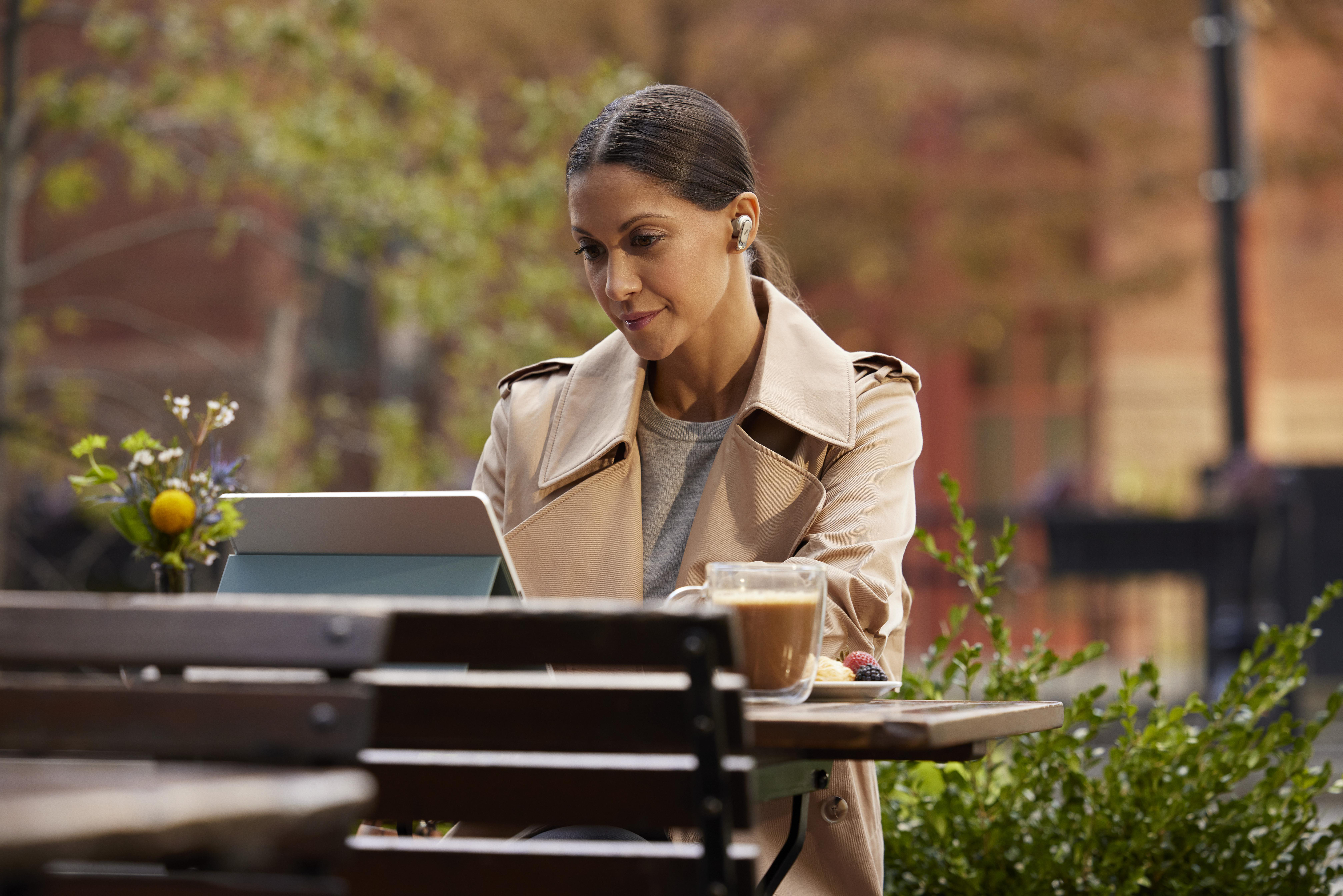 Eine Frau benutzt ein Tablet im Freien, sitzt an einem Tisch mit Kaffee und einem Snack.