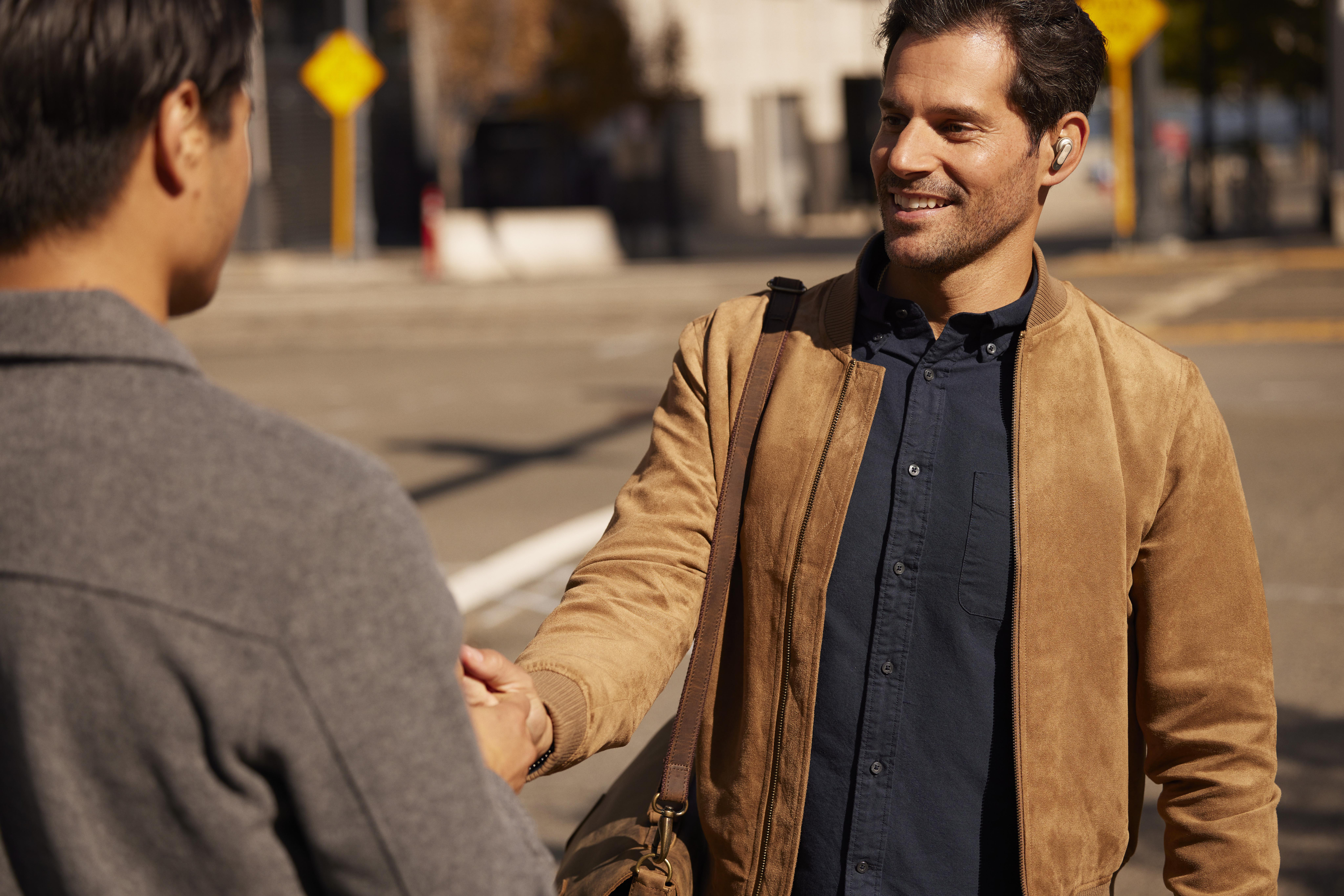 Zwei Männer geben sich im Freien die Hand. Einer trägt eine braune Jacke, der andere einen grauen Mantel.