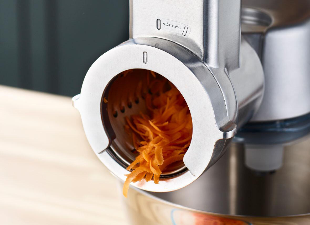 Nahaufnahme eines Zerkleinerers, der Karotten zerkleinert. Orangenfarbene Karottenschnitzel kommen aus dem Zerkleinerer.