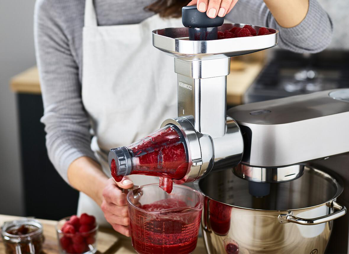 Eine Frau benutzt eine Küchenmaschine und verarbeitet Himbeeren. Saft fließt in einen Glasbehälter.