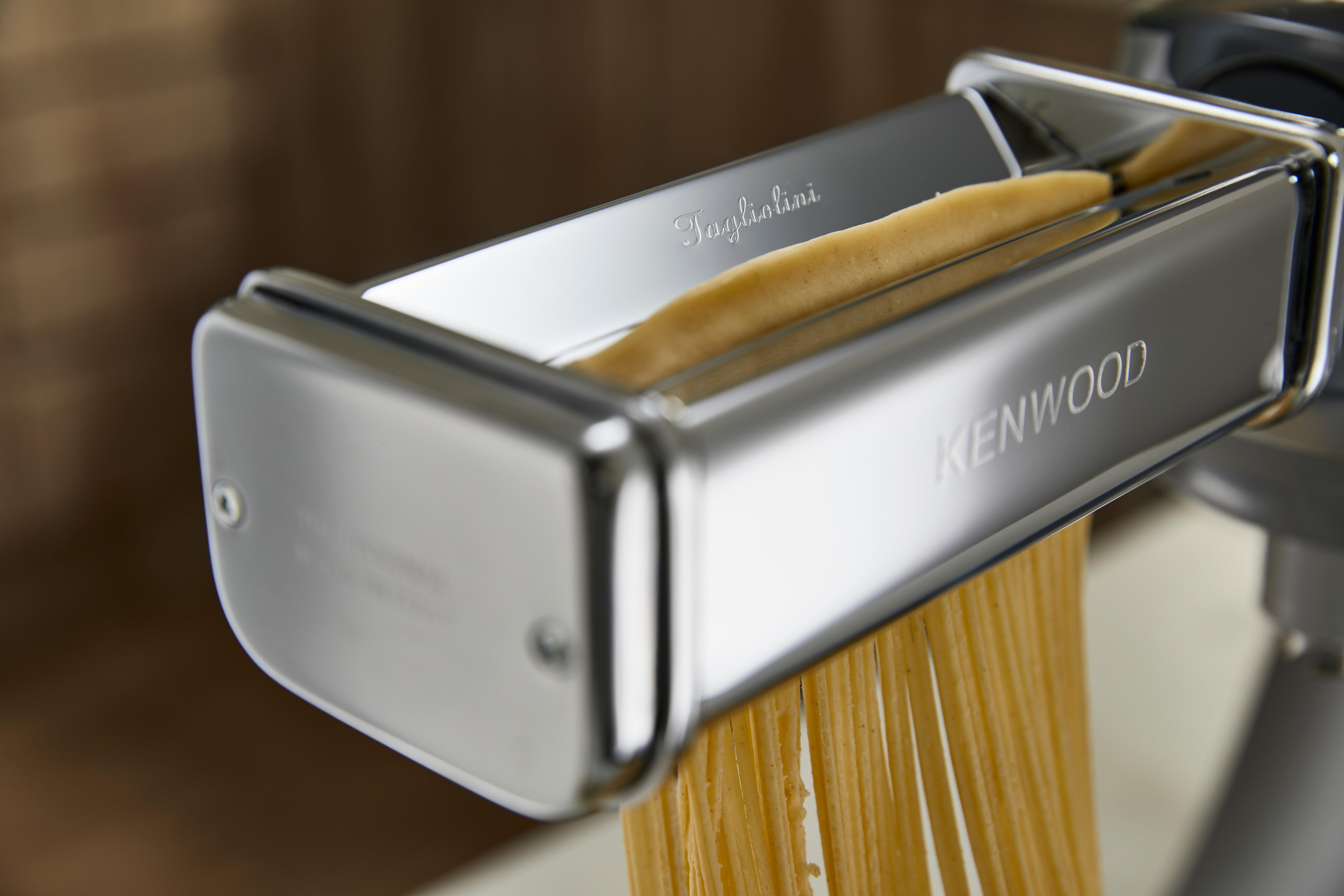 Eine Pastamaschine presst Tagliolini-Nudeln aus. Die Maschine ist silberfarben, das Wort "KENWOOD" ist sichtbar.