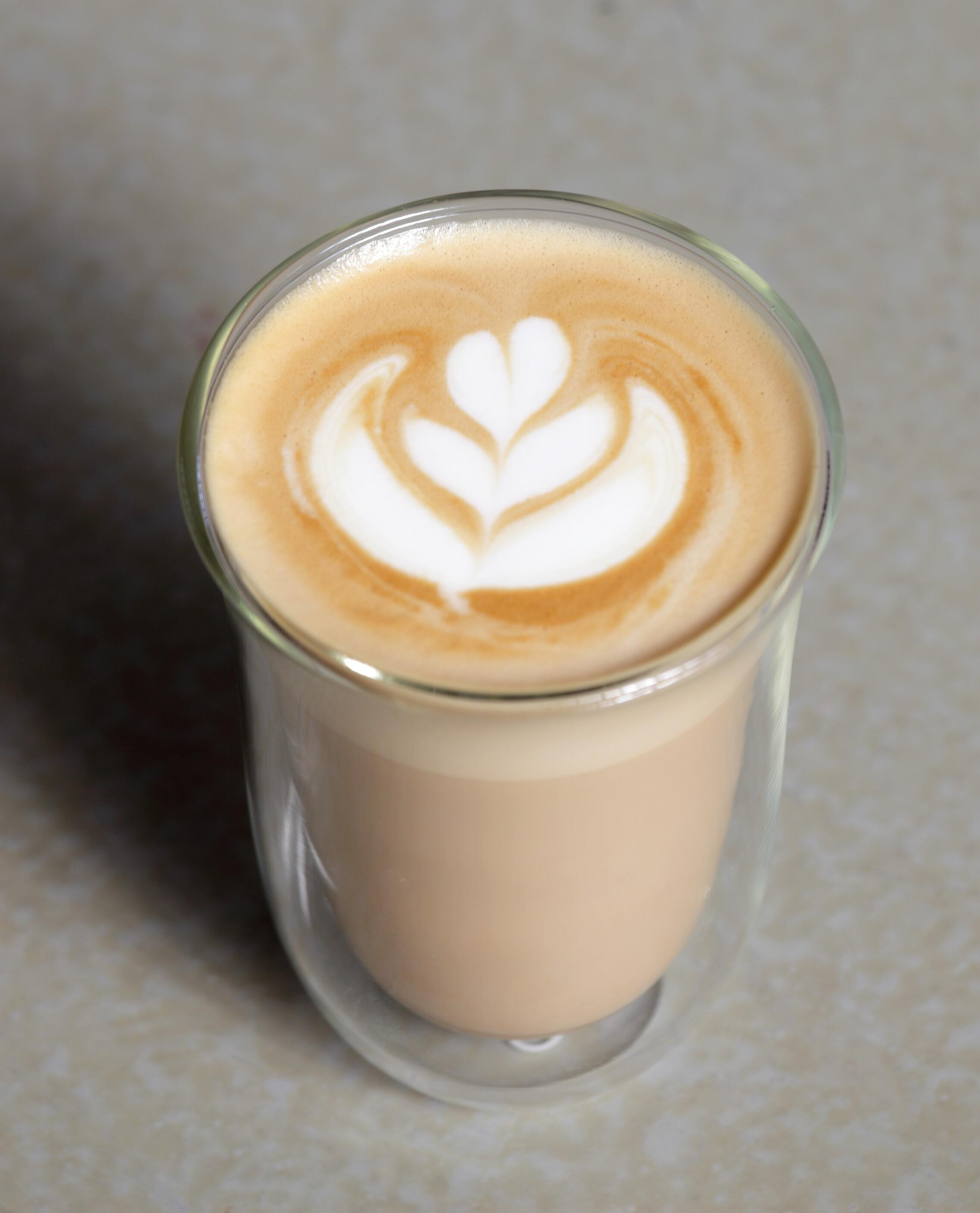 Nahaufnahme eines Latte Macchiato mit Latte Art in einem klaren Glas auf hellem Untergrund.