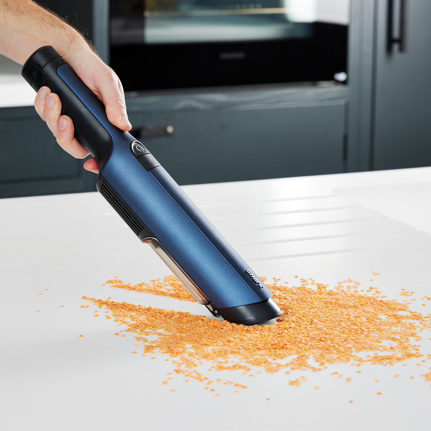 Hand vacuuming lentils from a white surface.