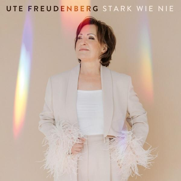 Frau in beigem Anzug schaut nach oben, mit farbenfrohem Licht. Text oben: 'UTE FREUDENBERG STARK WIE NIE'.
