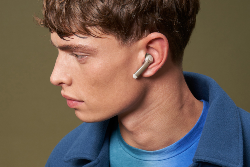 Un homme portant un écouteur dans son oreille. Il a les cheveux bruns et porte une chemise bleue.