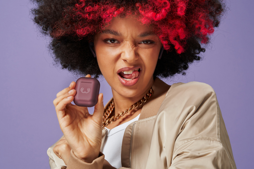 Une femme aux cheveux rouges tient un étui violet, tirant la langue.
