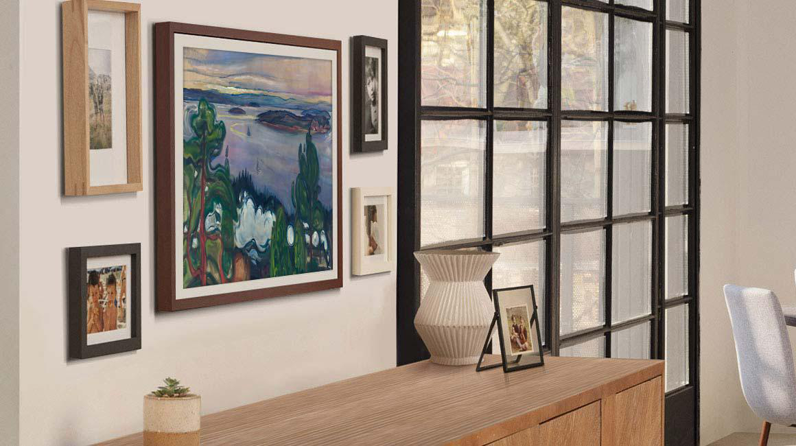 Innenwand mit mehreren gerahmten Kunstwerken und einer weißen Vase auf einem Holzschrank am Fenster.