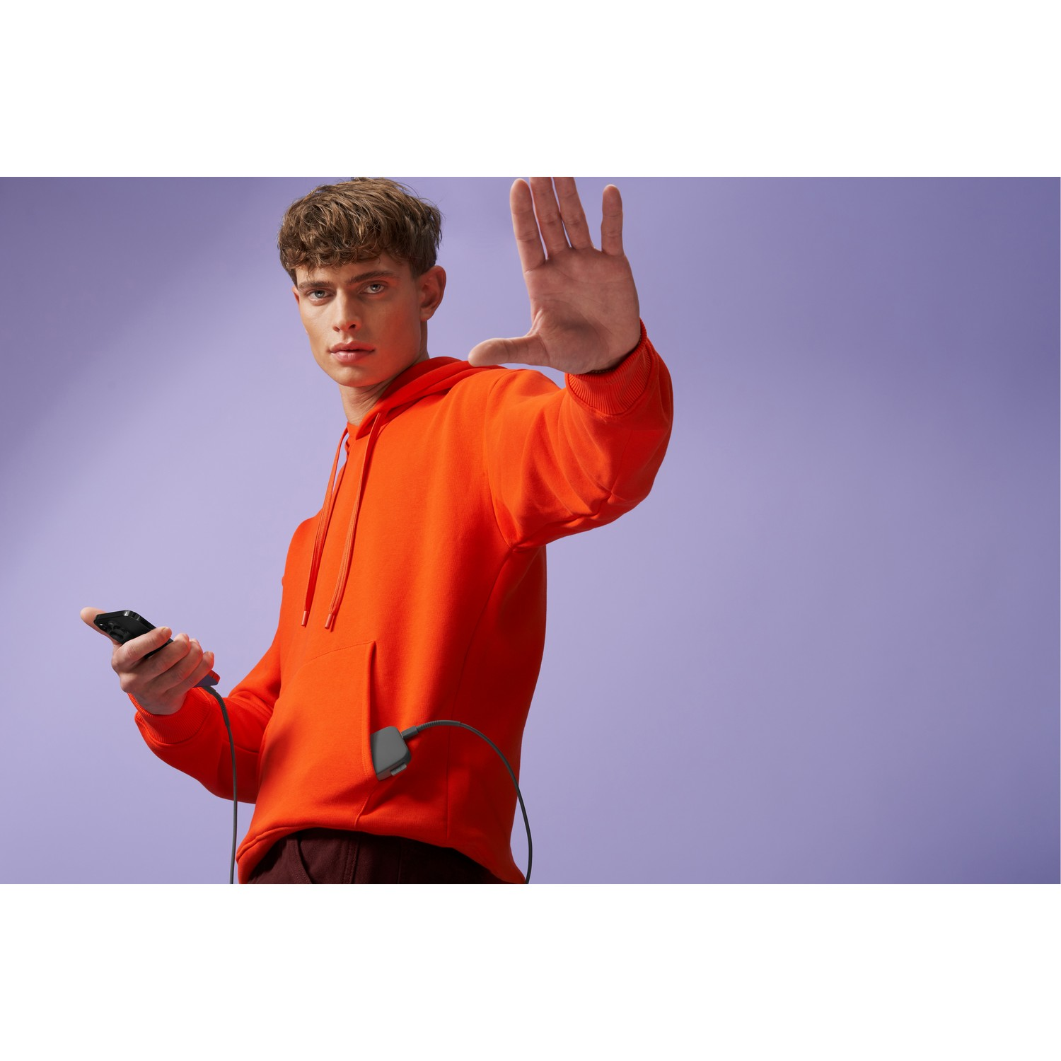 Een man in een oranje hoodie die een telefoon vasthoudt, met een oplaadkabel aangesloten.