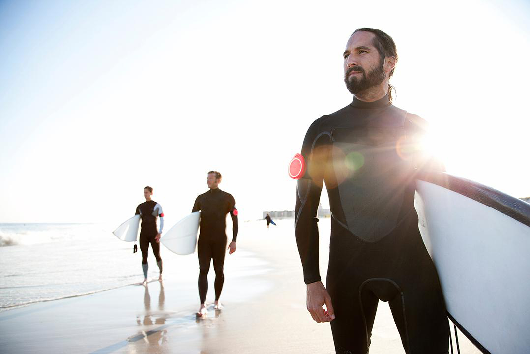 Drei Surfer am Strand, die auf das Wasser zulaufen. Einer hält ein Board und blickt nach vorn.