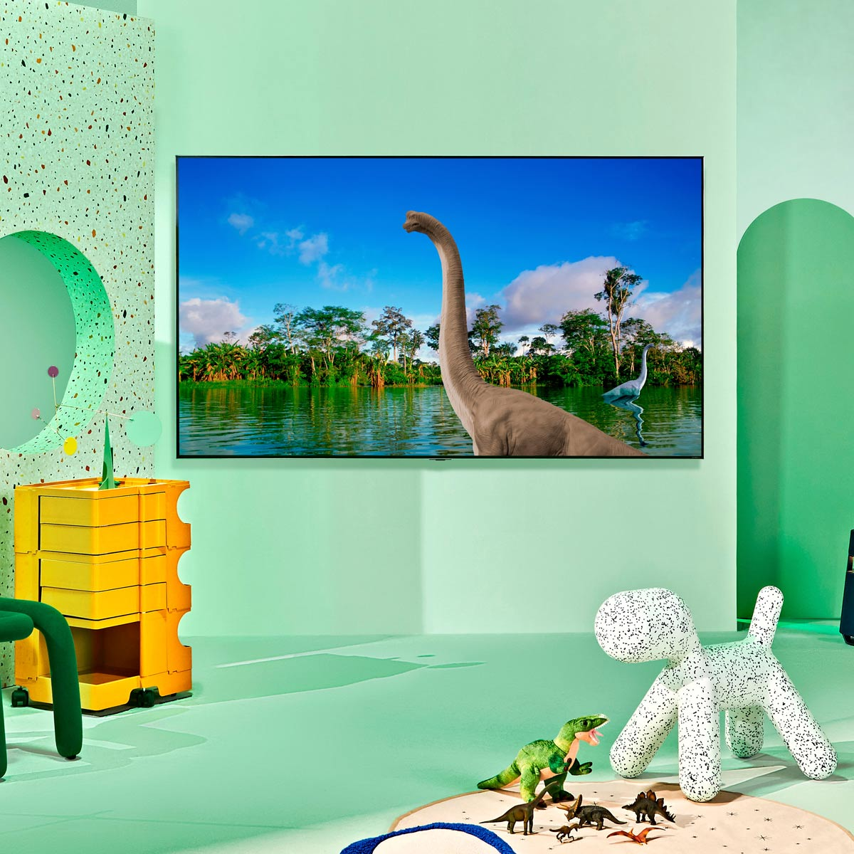 Un televisor muestra una escena de dinosaurios, con un braquiosaurio en un lago, en una habitación infantil.
