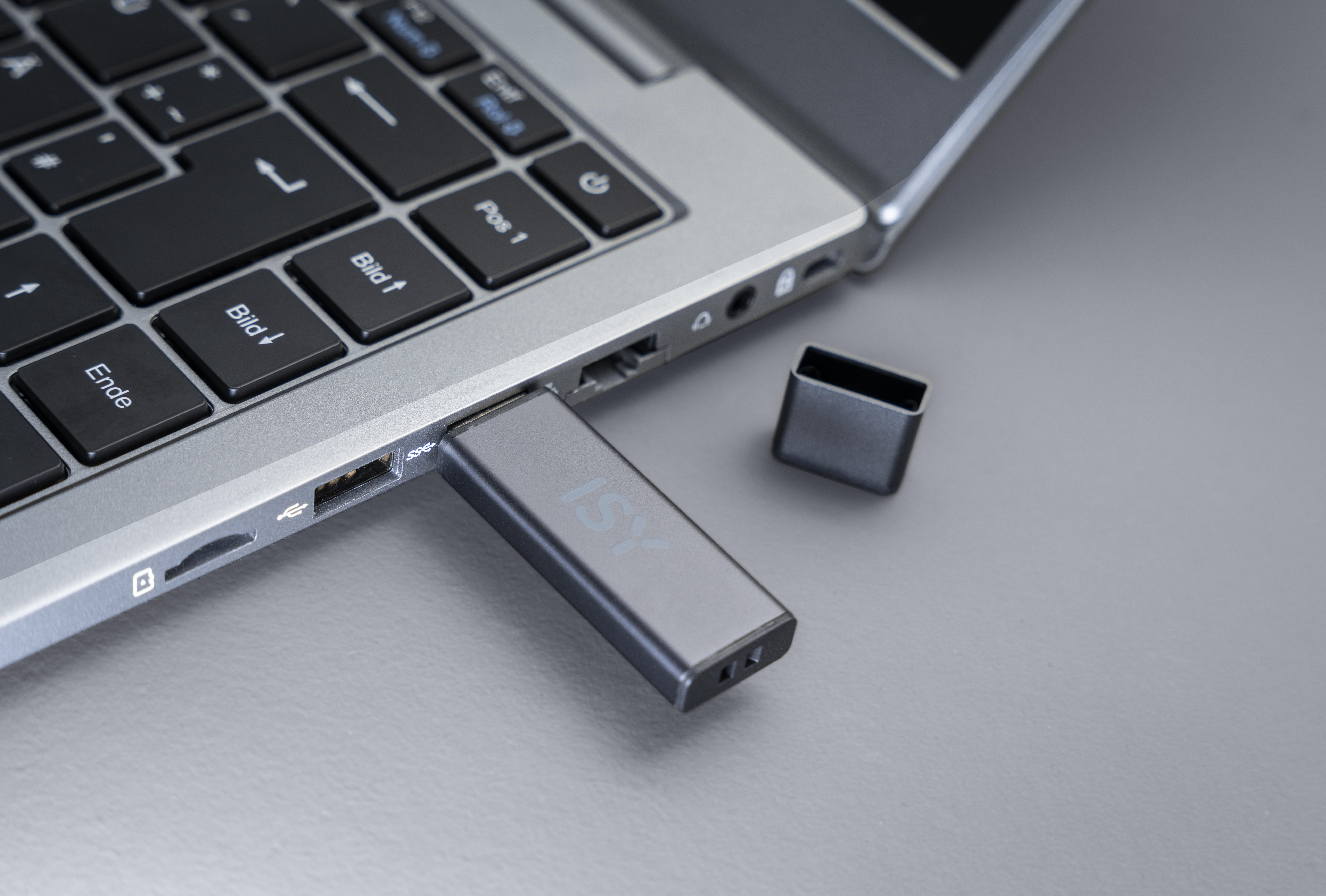 Ein grauer USB-Stick, der in einen Laptop gesteckt ist, mit der Kappe daneben.