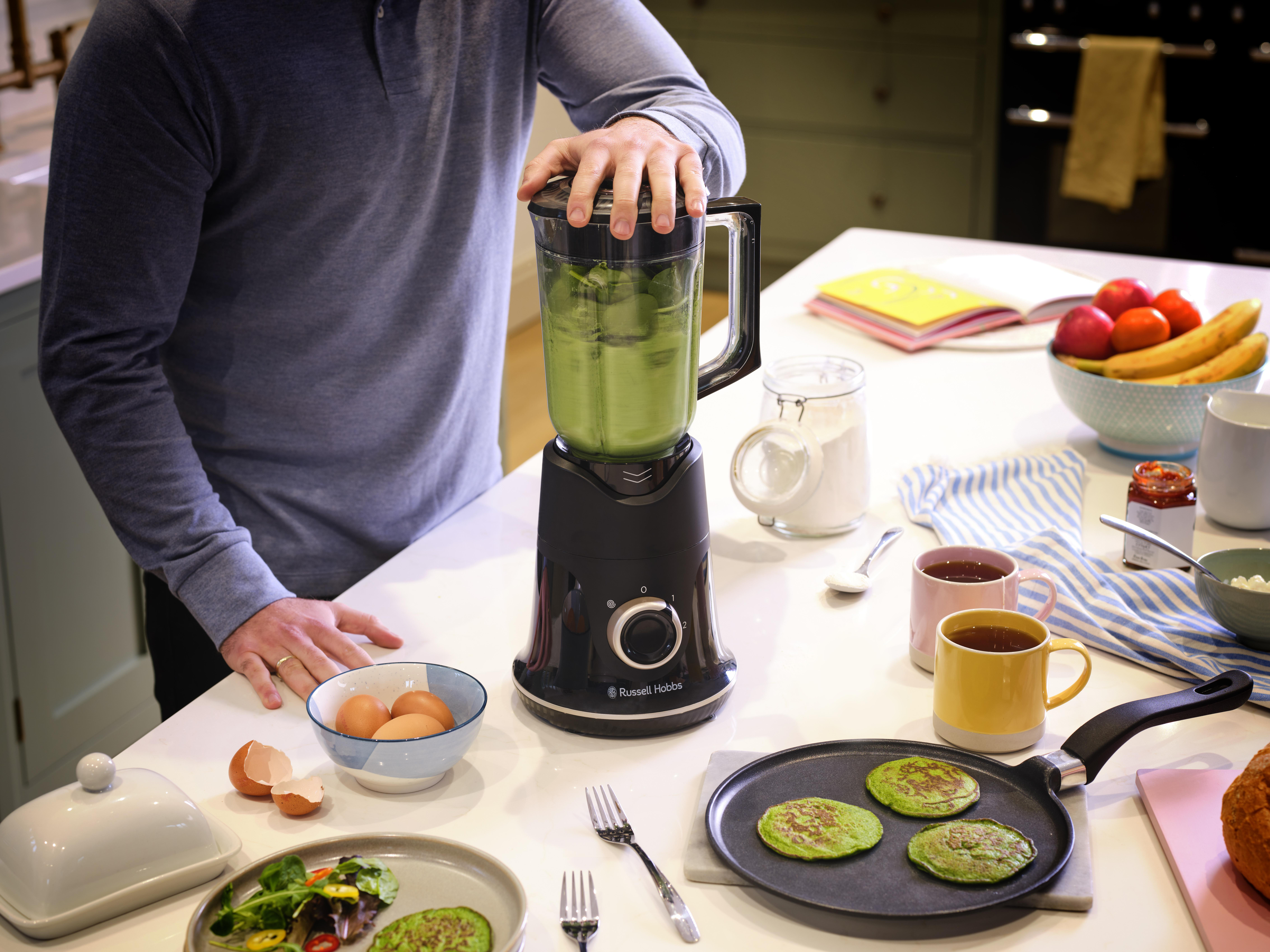 Mann in einer Küche, der einen grünen Smoothie in einem Mixer zubereitet.