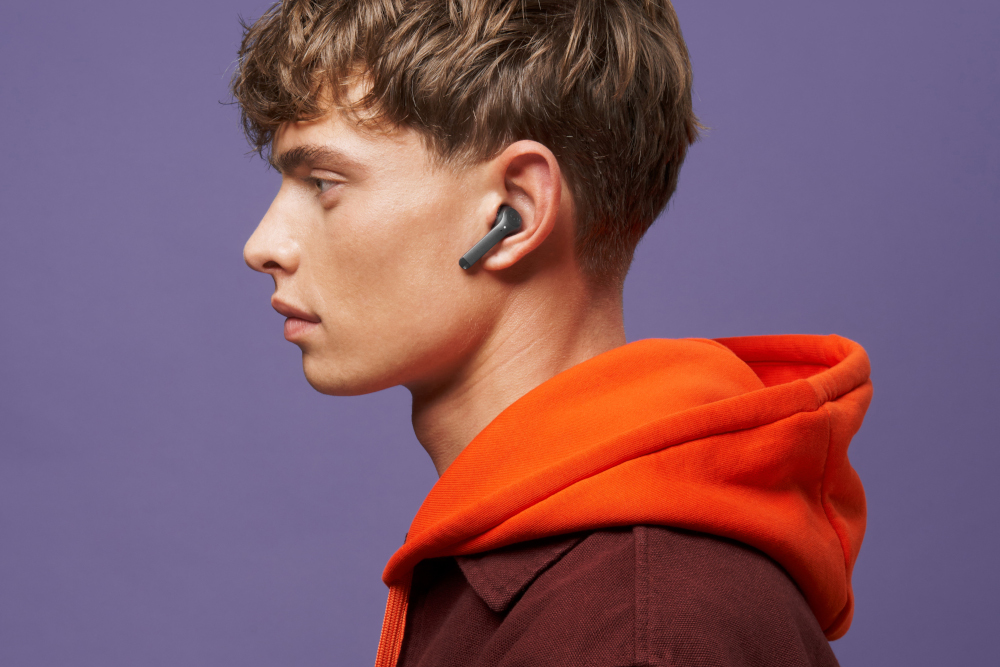 A man with earbuds in ear, wearing an orange hoody.