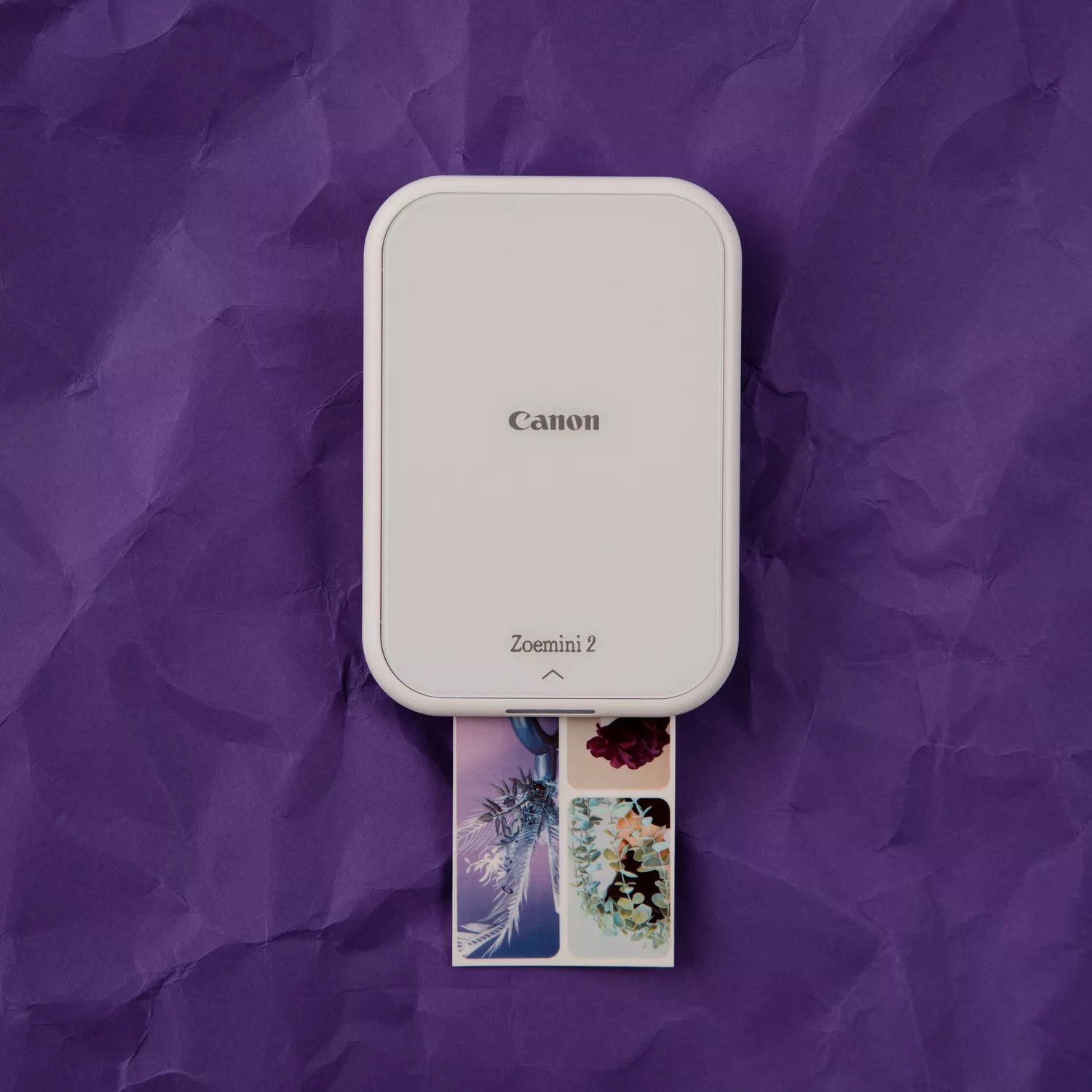 Weißer Canon Zoemini 2 Drucker auf lila Papier, druckt Fotos mit floralen Bildern.