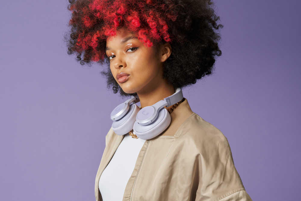 Vrouw met rood-gestreept zwart haar, draagt jas en koptelefoon.